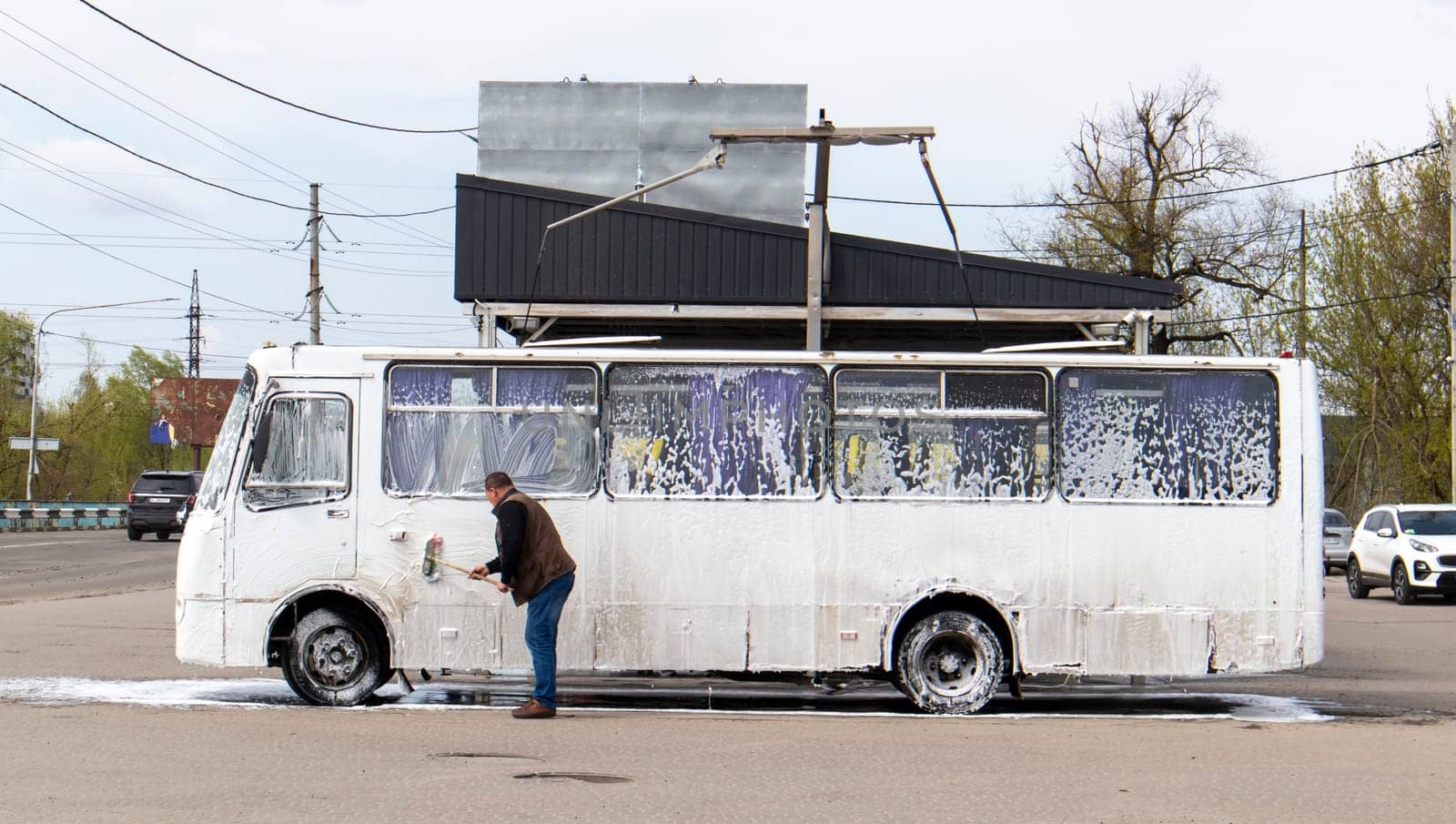 Big white bus in foam at a self-service car wash. External washing of public transport buses. Self-service manual high-pressure car wash in the open air
