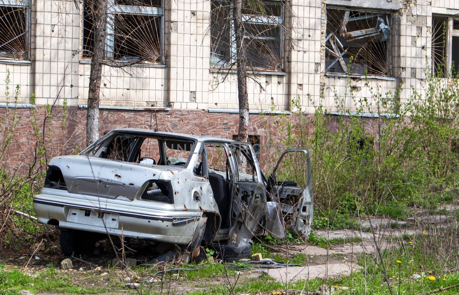 The car that burned down after the bombing of the city stands in the courtyard of a destroyed house. War between Russia and Ukraine. Fragments of a car after artillery shelling