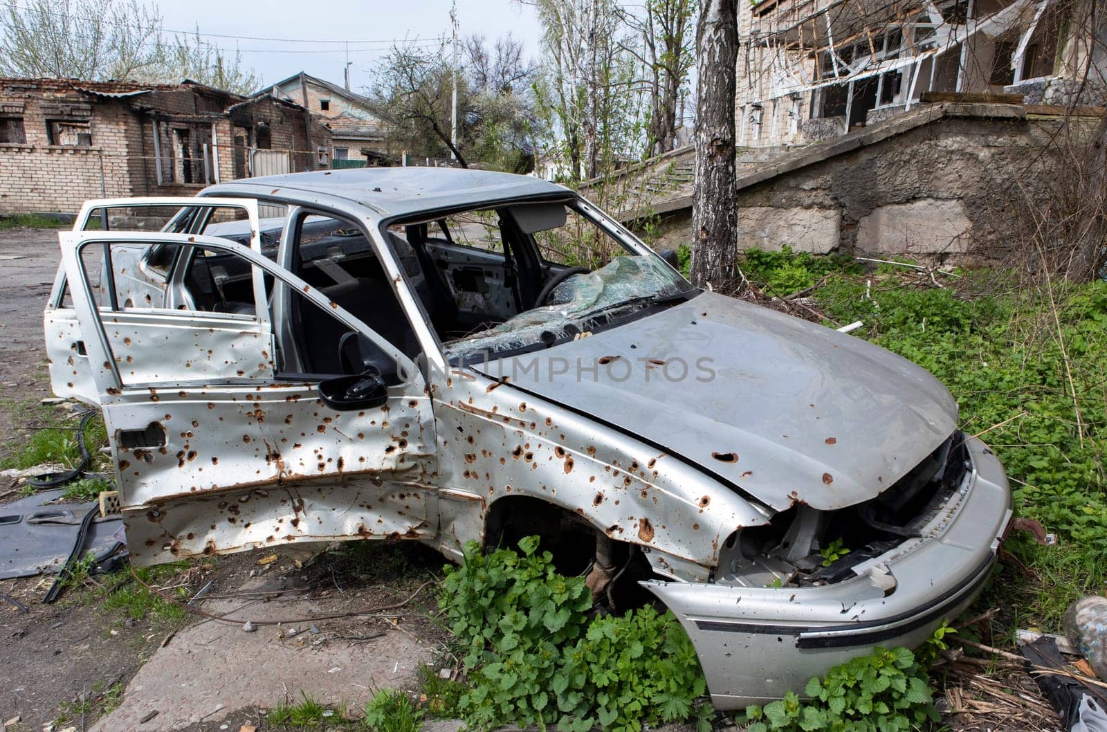 The car that burned down after the bombing of the city stands in the courtyard of a destroyed house. War between Russia and Ukraine. Fragments of a car after artillery shelling