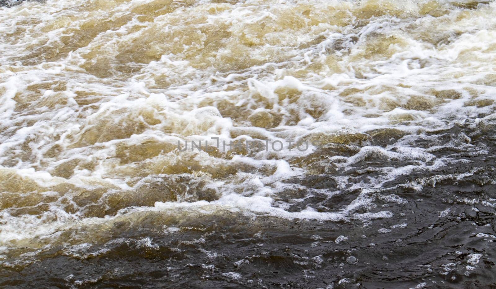 River rapids. Close up abstract background of falling water. Water flows over river rocks. A beautiful powerful stream of a stormy mountain river. The river rushes with fast-flowing water