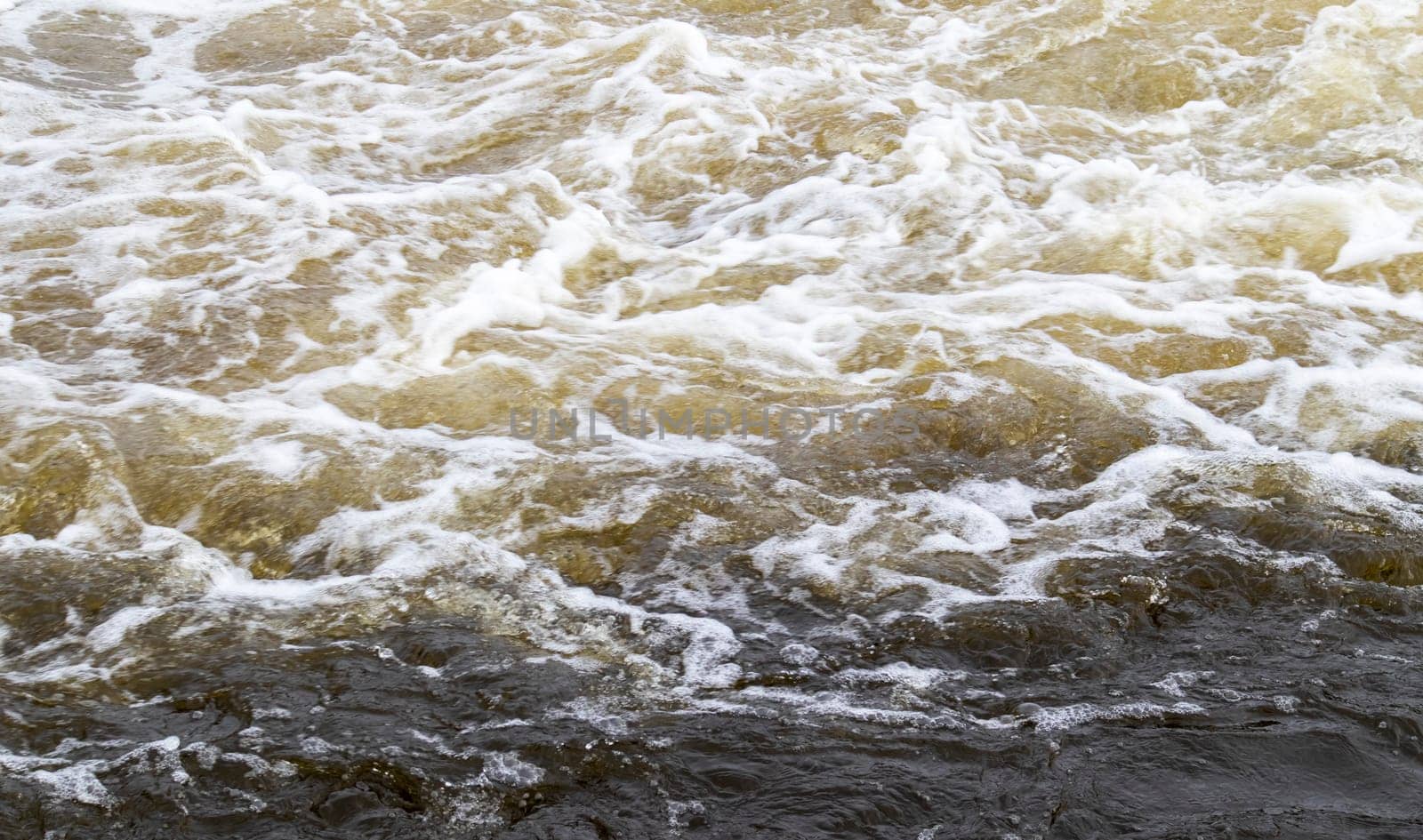 River rapids. Close up abstract background of falling water. Water flows over river rocks. A beautiful powerful stream of a stormy mountain river. The river rushes with fast-flowing water