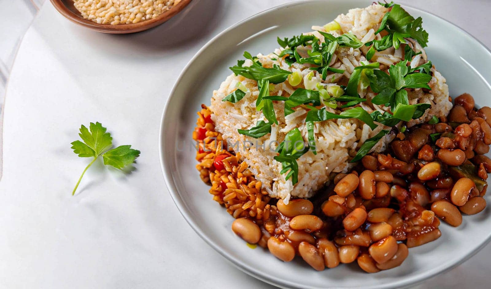 Pan-fried shrimp and blend of couscous, orzo, garbanzo beans, and red quinoa served with green peas and green onion close up on a plate on white background