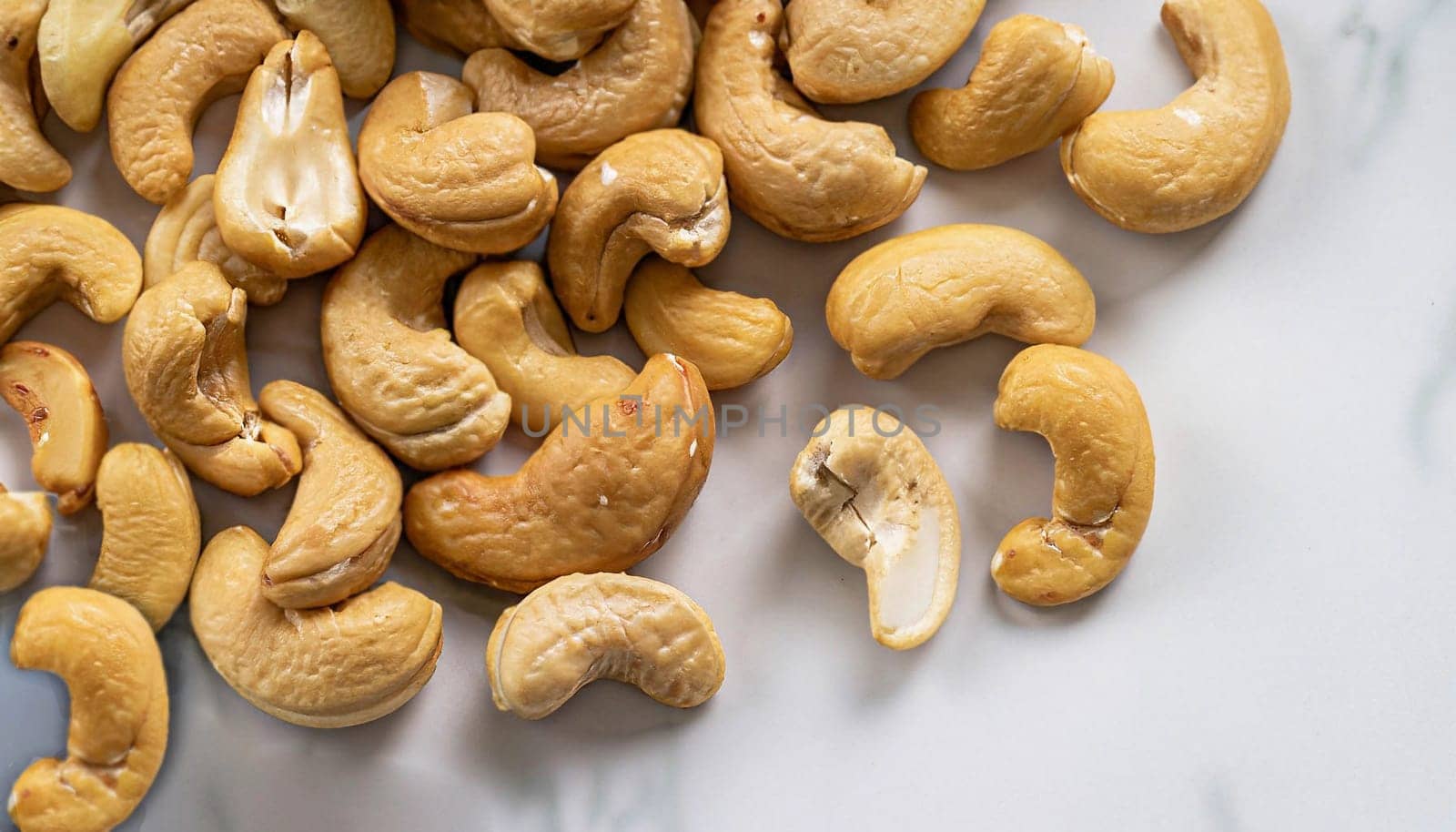 A pile of roasted cashew nuts scattered on a white marble background