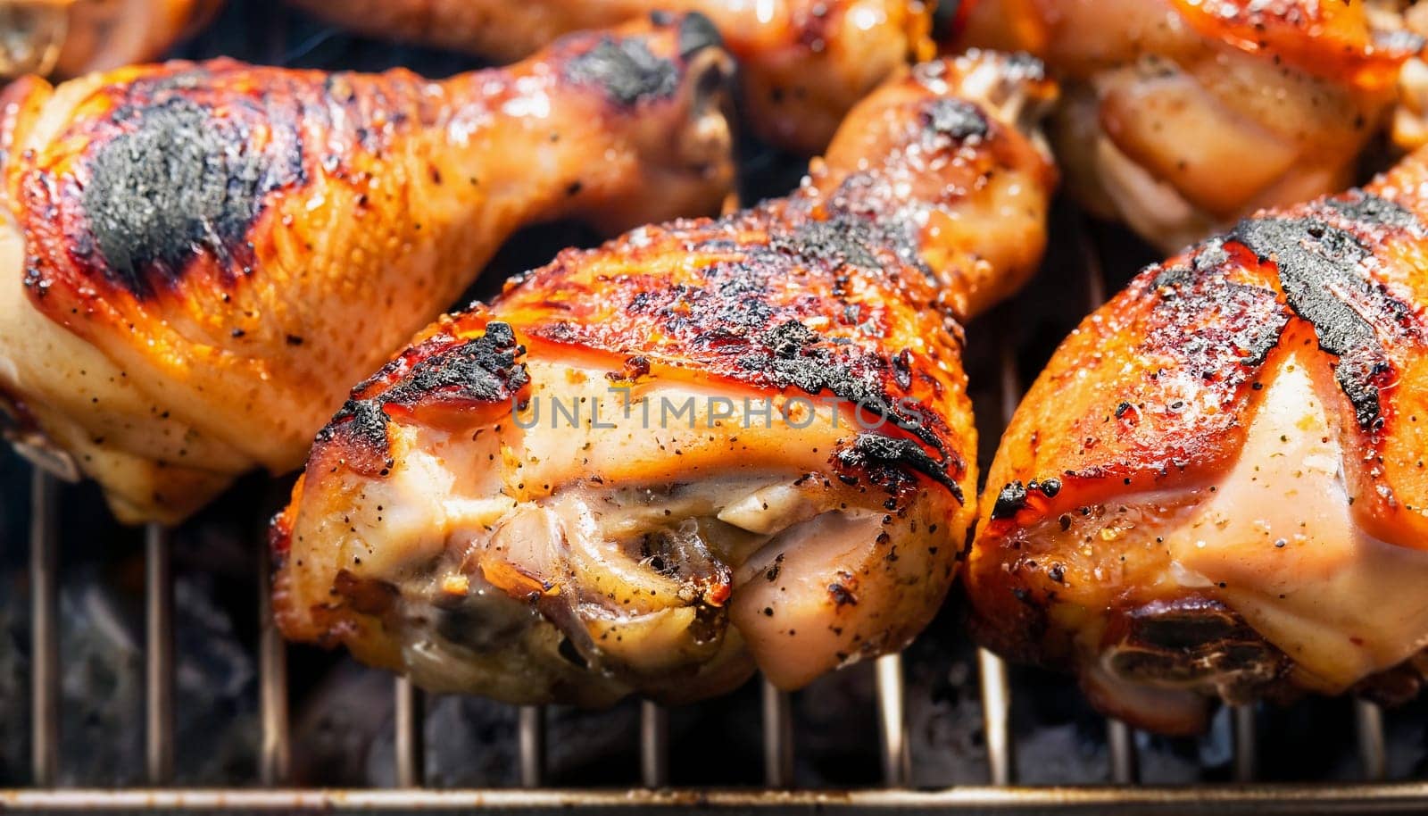 Chicken grilled charcoal on a black iron grill. The chicken is light yellow to dark yellow with white bones.