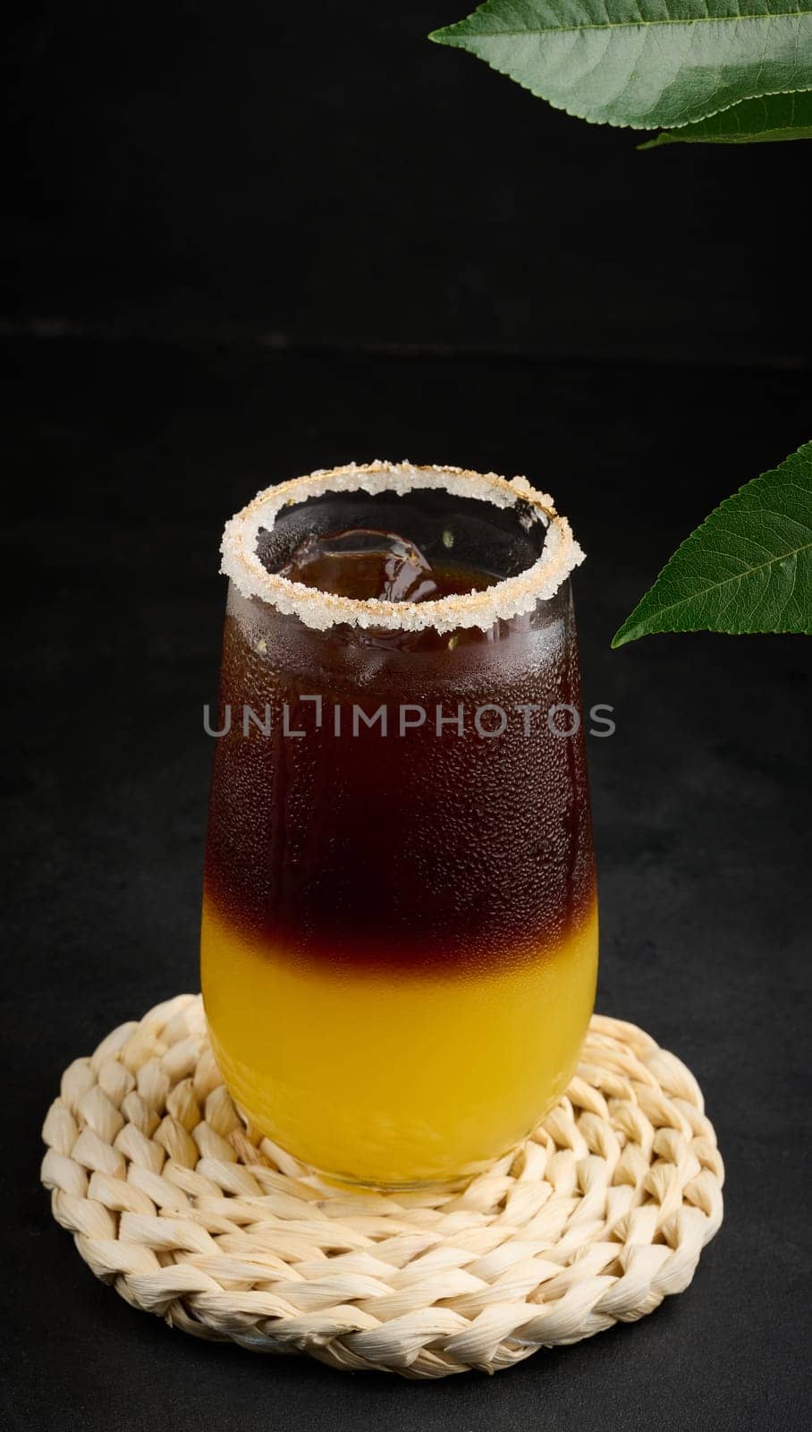 Iced coffee with orange juice in a transparent glass, refreshing bumble coffee on the table, black background