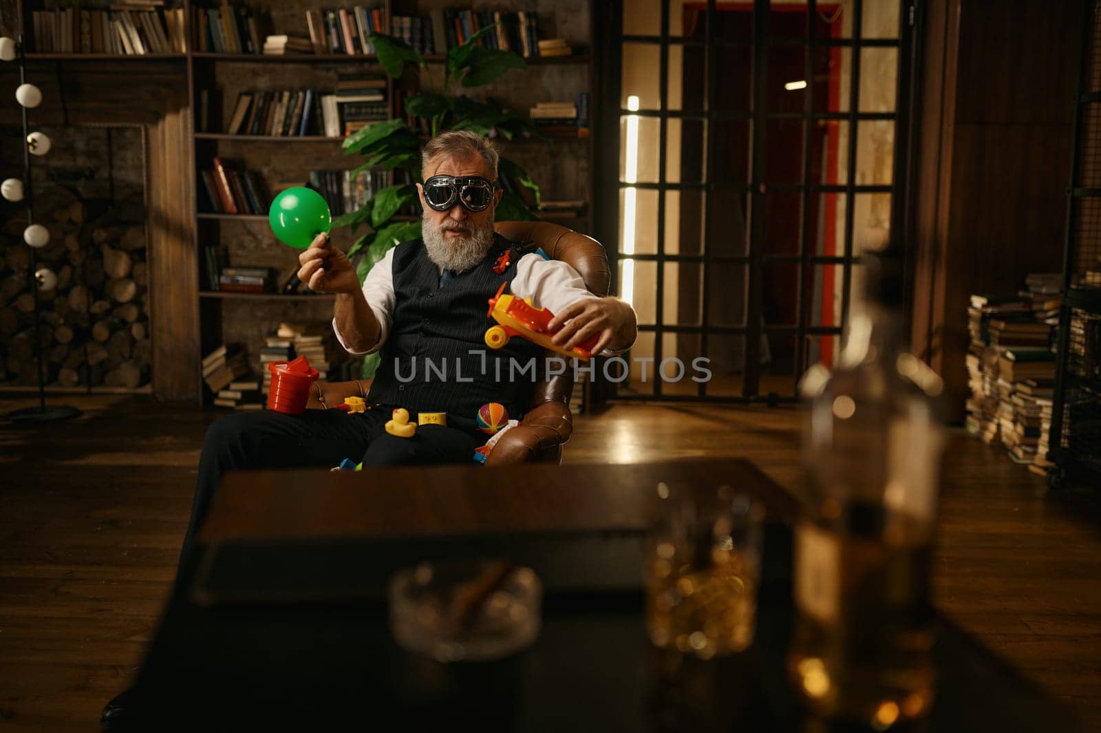 Selective focus of rich elegant senior businessman playing toys at home office. Elderly mature male character wearing elegant suit and pilot goggles having fun and rest after hard work day