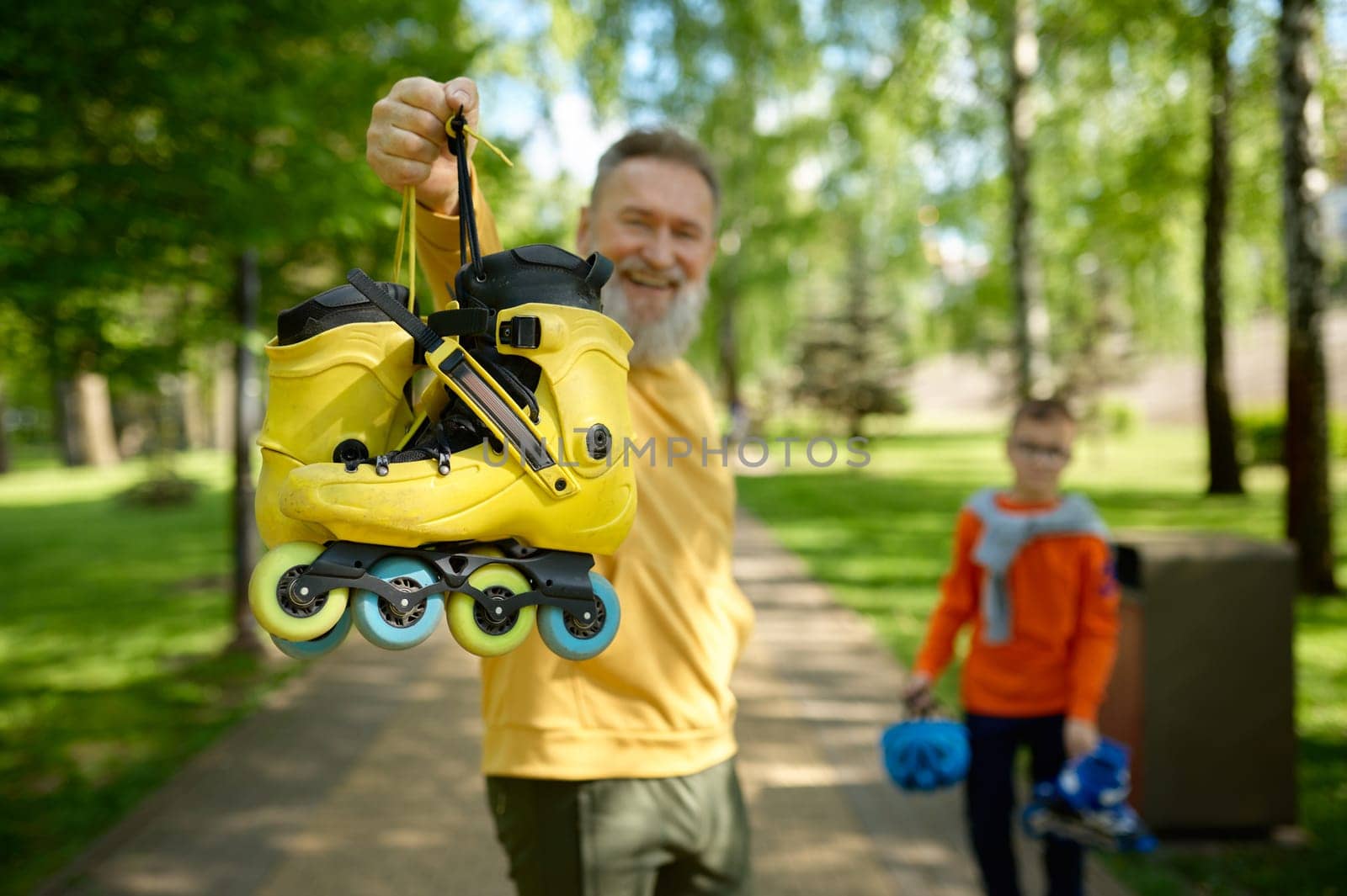 Happy grandparent and grandchild getting ready for extreme riding and active sports pastime in park. Selective focus of roller-skate