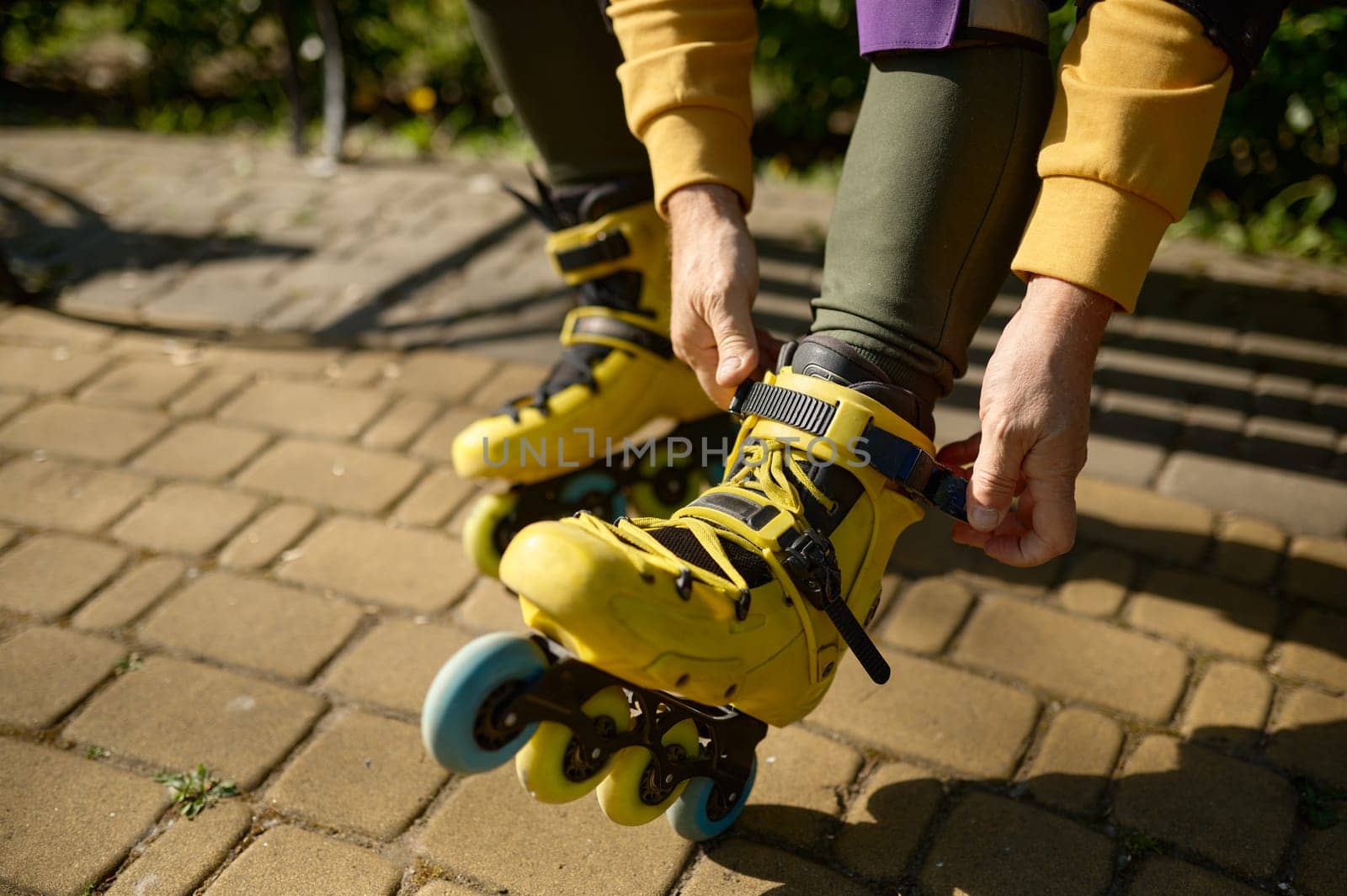 Closeup view of man putting on roller skates while sitting on bench in park. Active recreation time, lifestyle concept