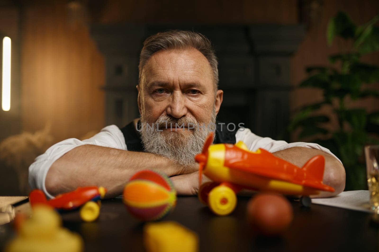 Portrait of thoughtful senior businessman with toys while rest at workplace in home office. Elderly male having fun enjoying stress relief entertainment