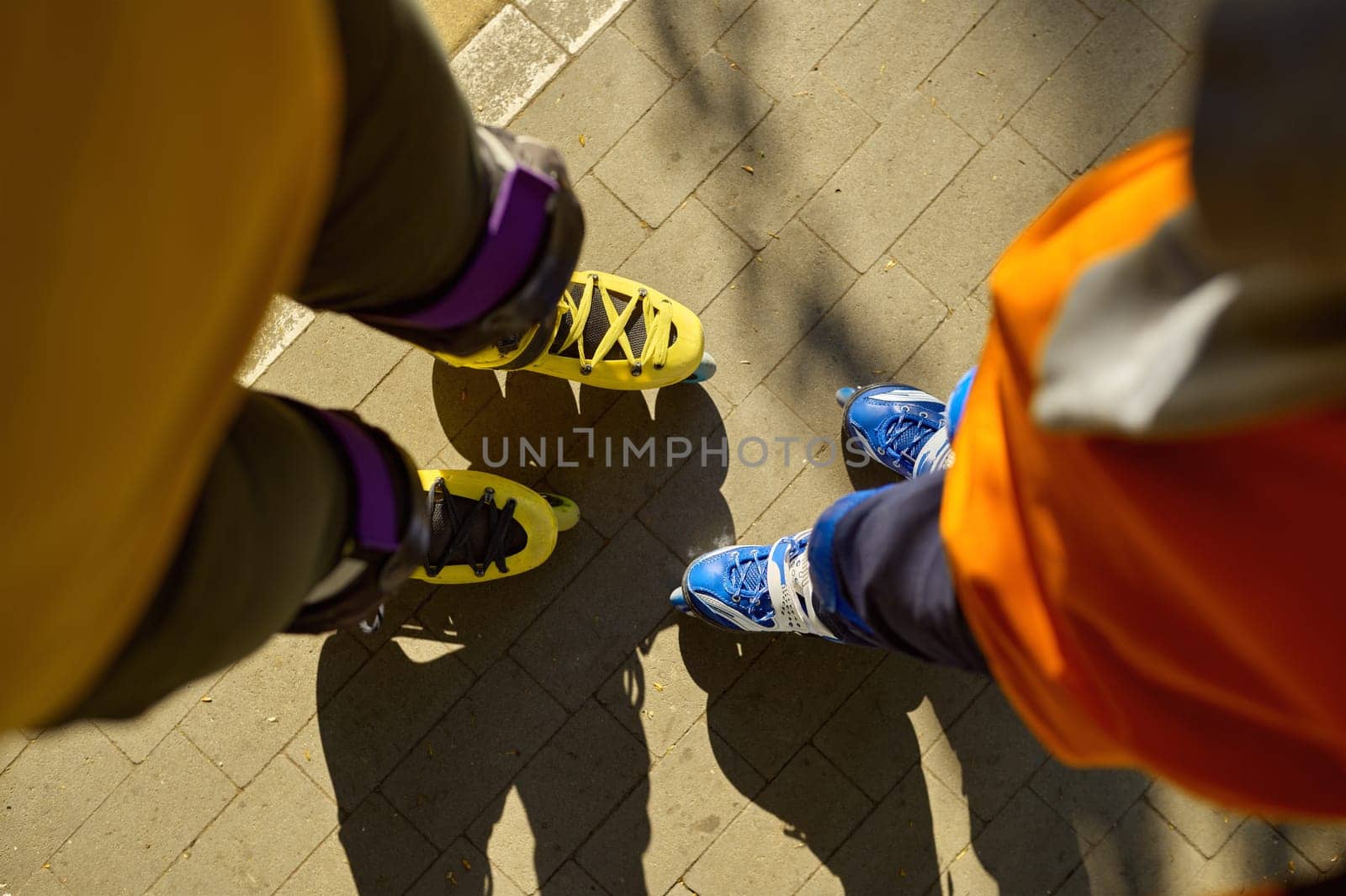 Cropped top view shot of man and boy legs wearing rollerblades over city park background. Active recreation time and sports activity in summer