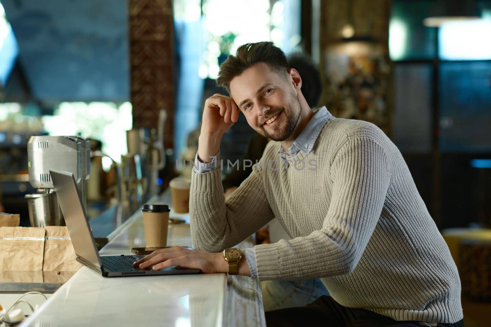 Happy male IT professional using laptop computer working in coworking space. Office worker watching virtual webinar or online training, having meeting by video chat app
