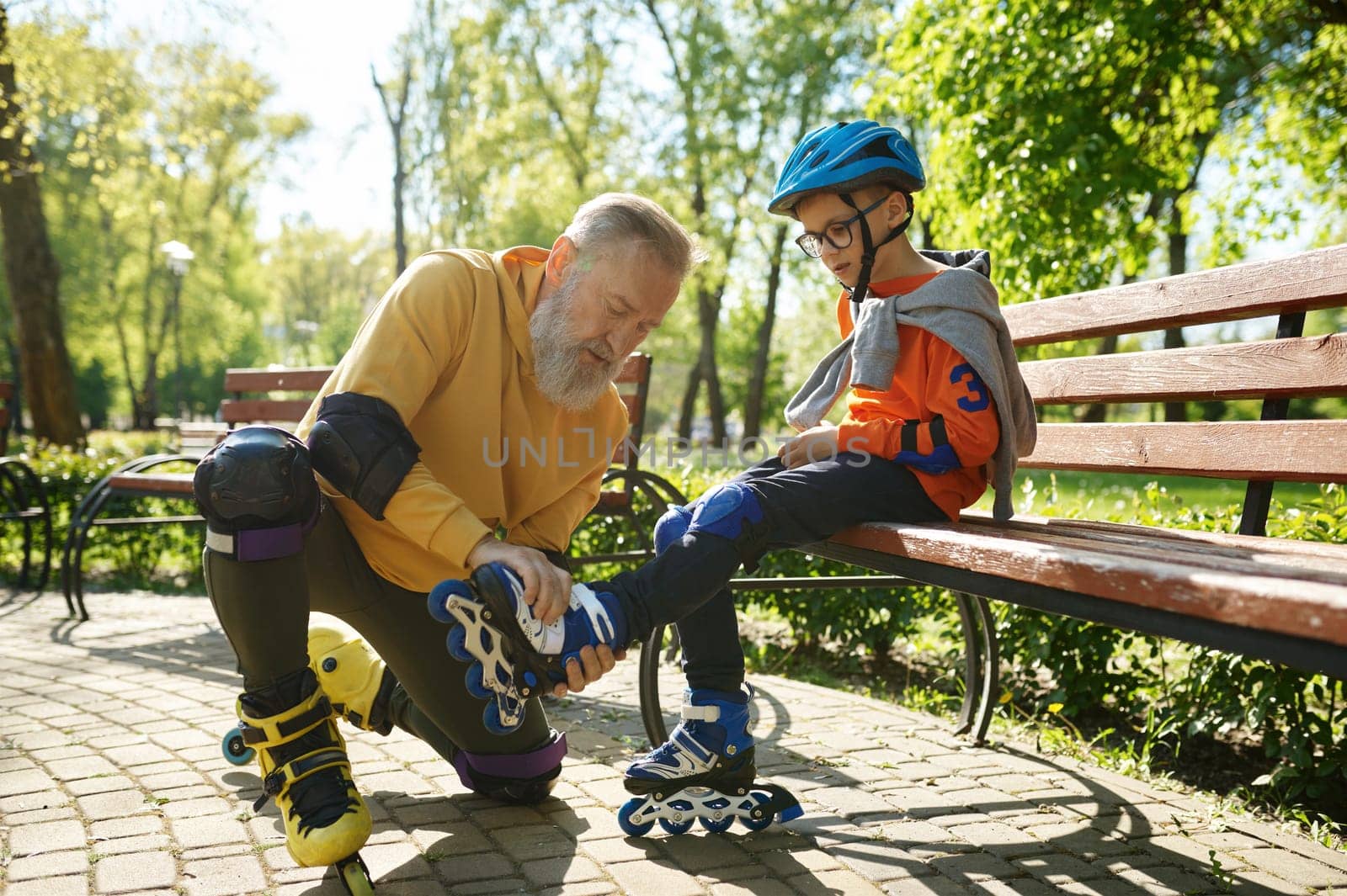Father helping son to put on roller skates. Happy family active rest and leisure recreation time in urban park on weekend