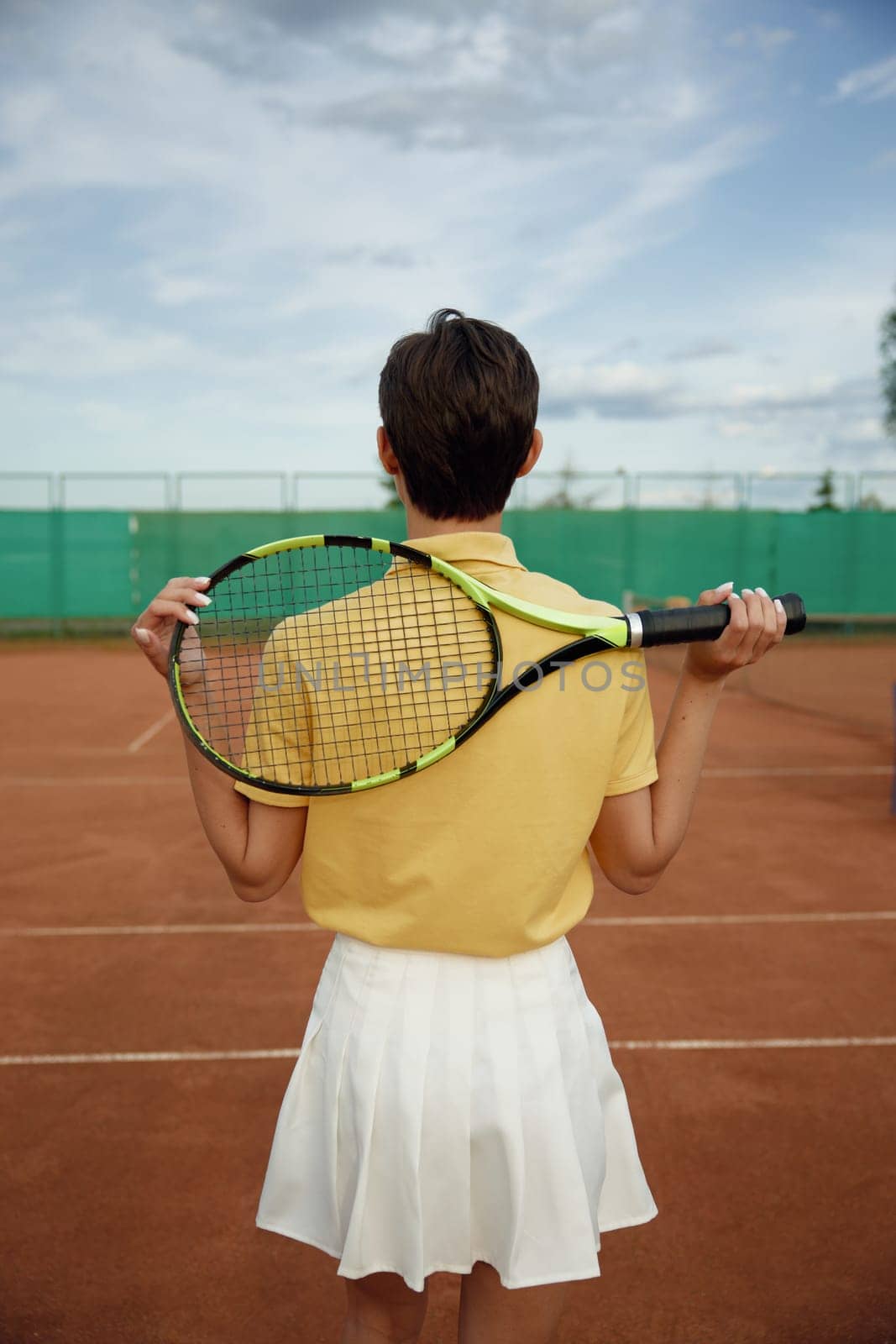 Back view on young teenage woman tennis player holding racket on shoulders. Recreational activity and professional sport concept