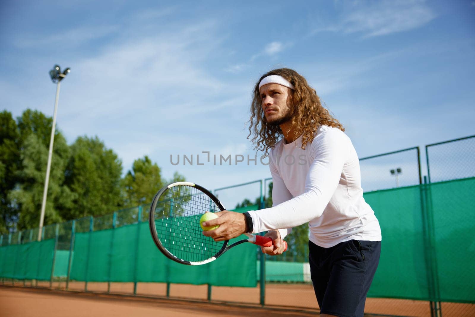 Concentrated male tennis player with racket and ball training on outdoor court. Preparation for serving