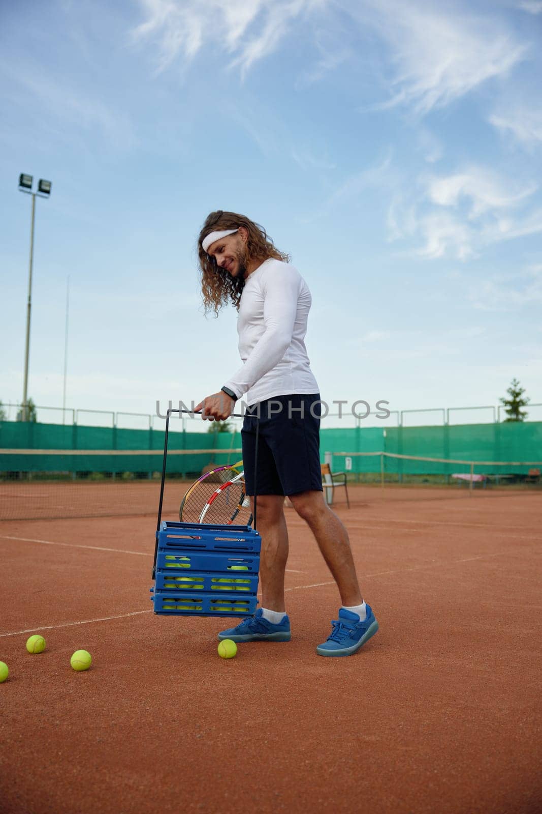 Young satisfied tennis player picking up scattered balls on field after game training. Professional occupation or hobby recreation concept