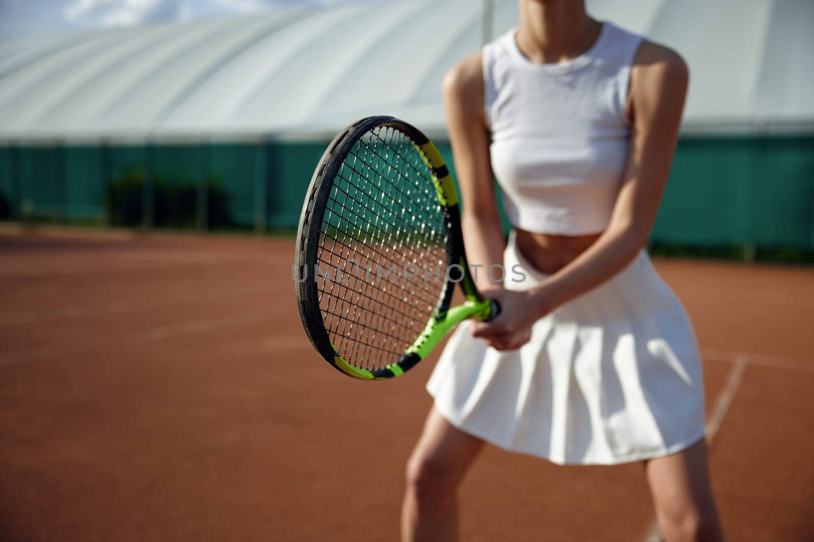 Closeup view on female tennis player holding racket. Sportswoman ready to return ball. Outdoor sport activity concept