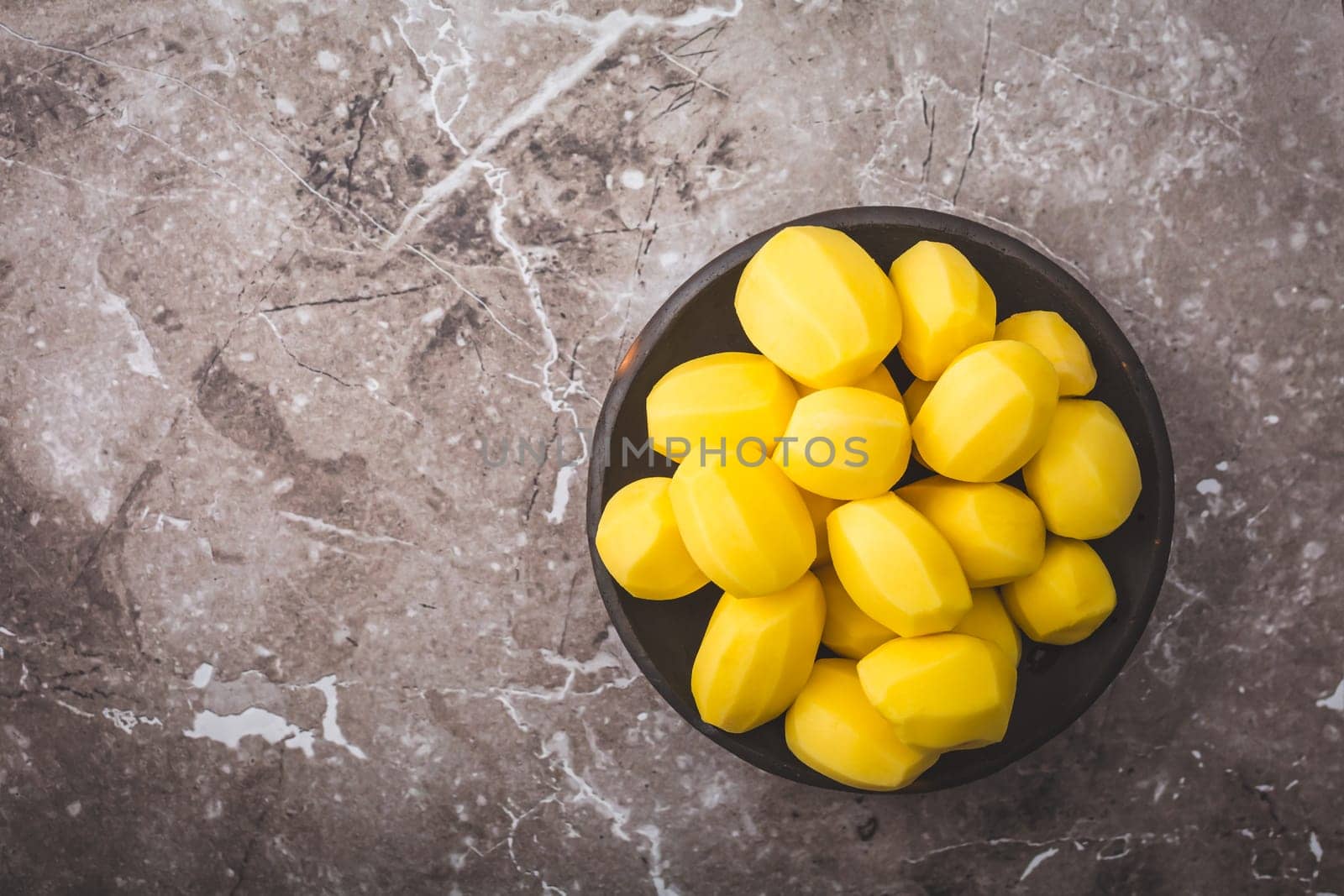 Raw peeled potatoes in a bowl on kitchen table