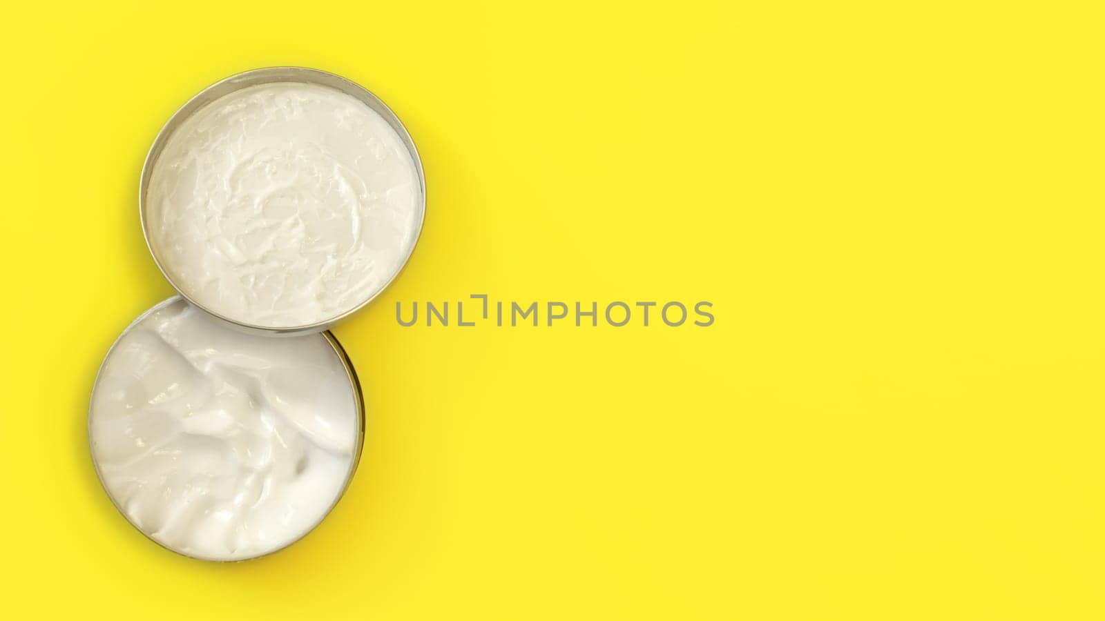 Tabletop view, metal round tin container with white cosmetic cream on yellow board, cap over the jar base, wide banner with text space right