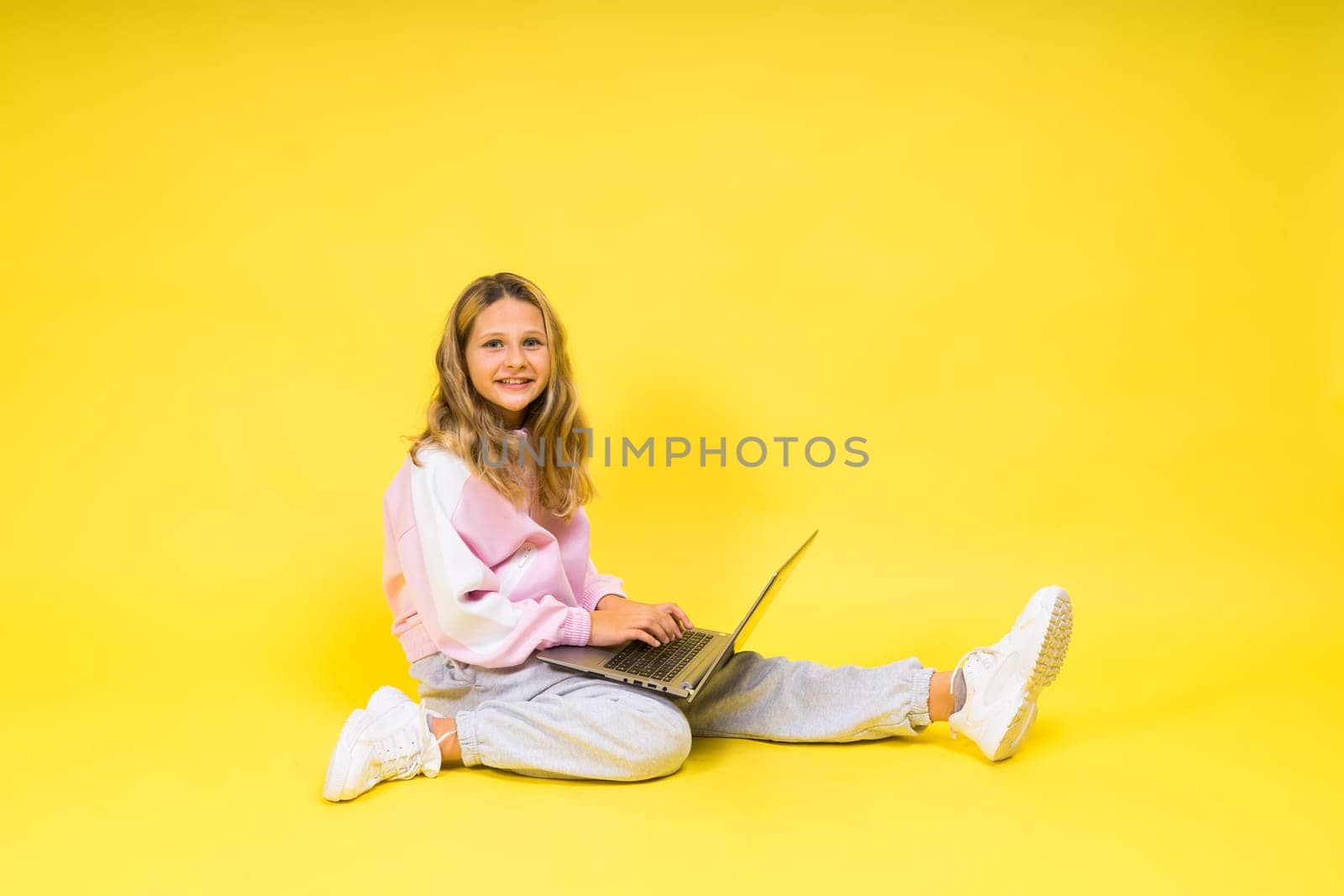 Positive kid sit with a laptop read homework wear casual style cloth isolated over yellow background