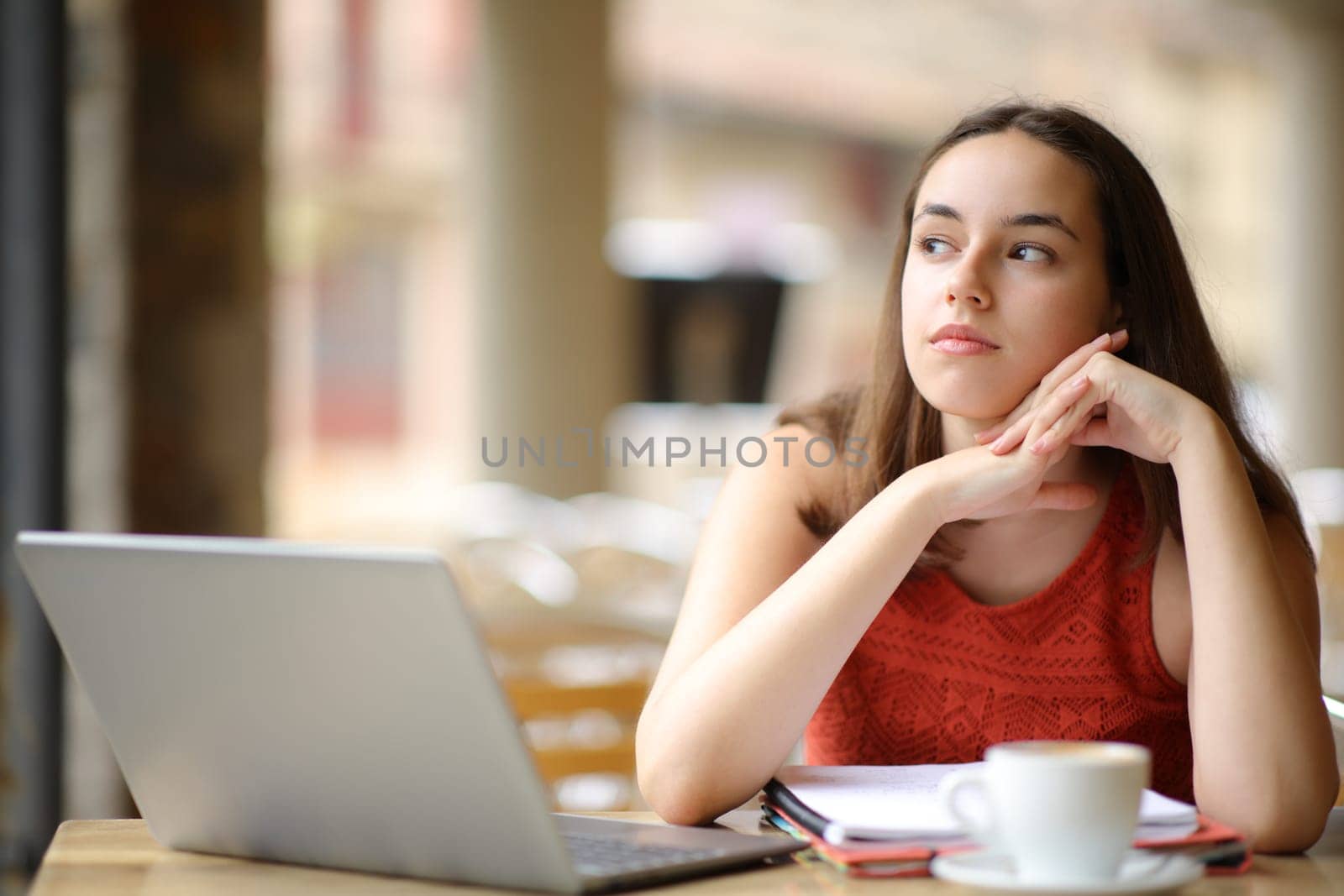 Distracted student thinking looking at side in a coffee shop terrace