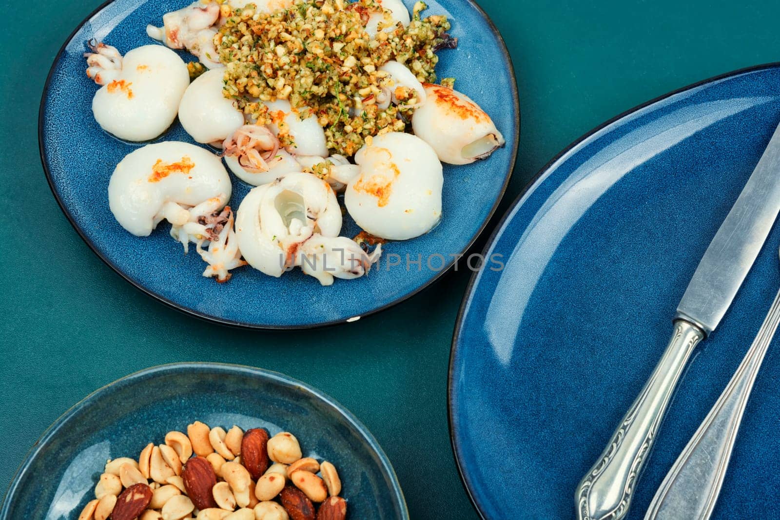 Baked young squids served with nut salad on wooden table.