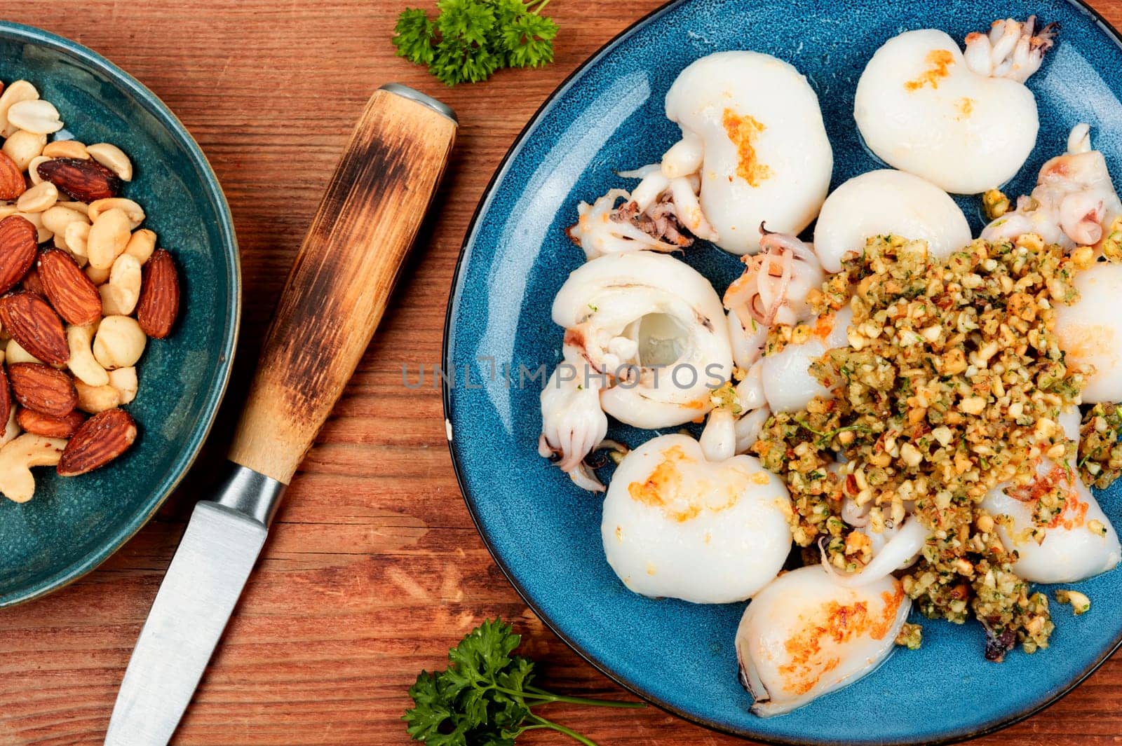 Baked young squids served with nut salad on wooden table.