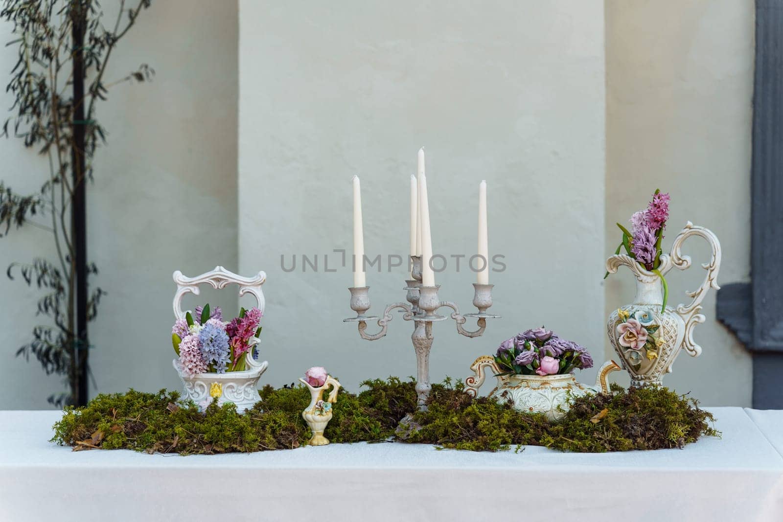 Decorative decoration of the festive table. Candlestick with candles, vases with hyacinths and other flowers, green moss on a table covered with a white tablecloth.