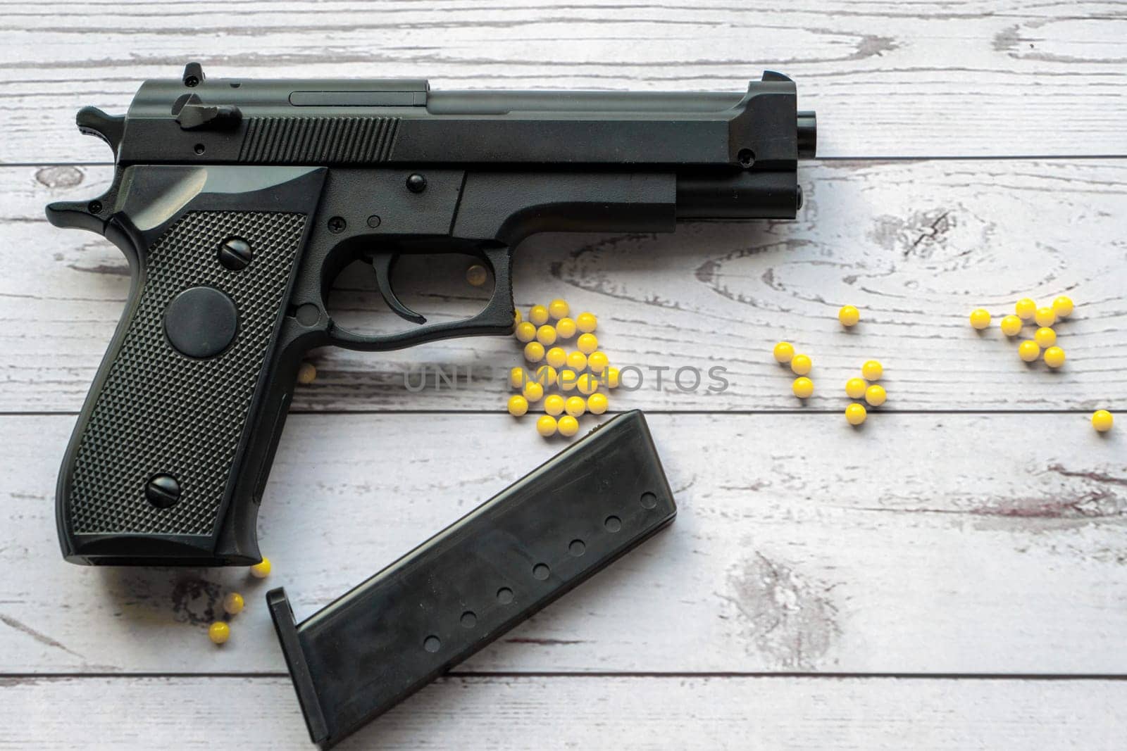 airsoft handgun with yellow bb, on a white wooden background