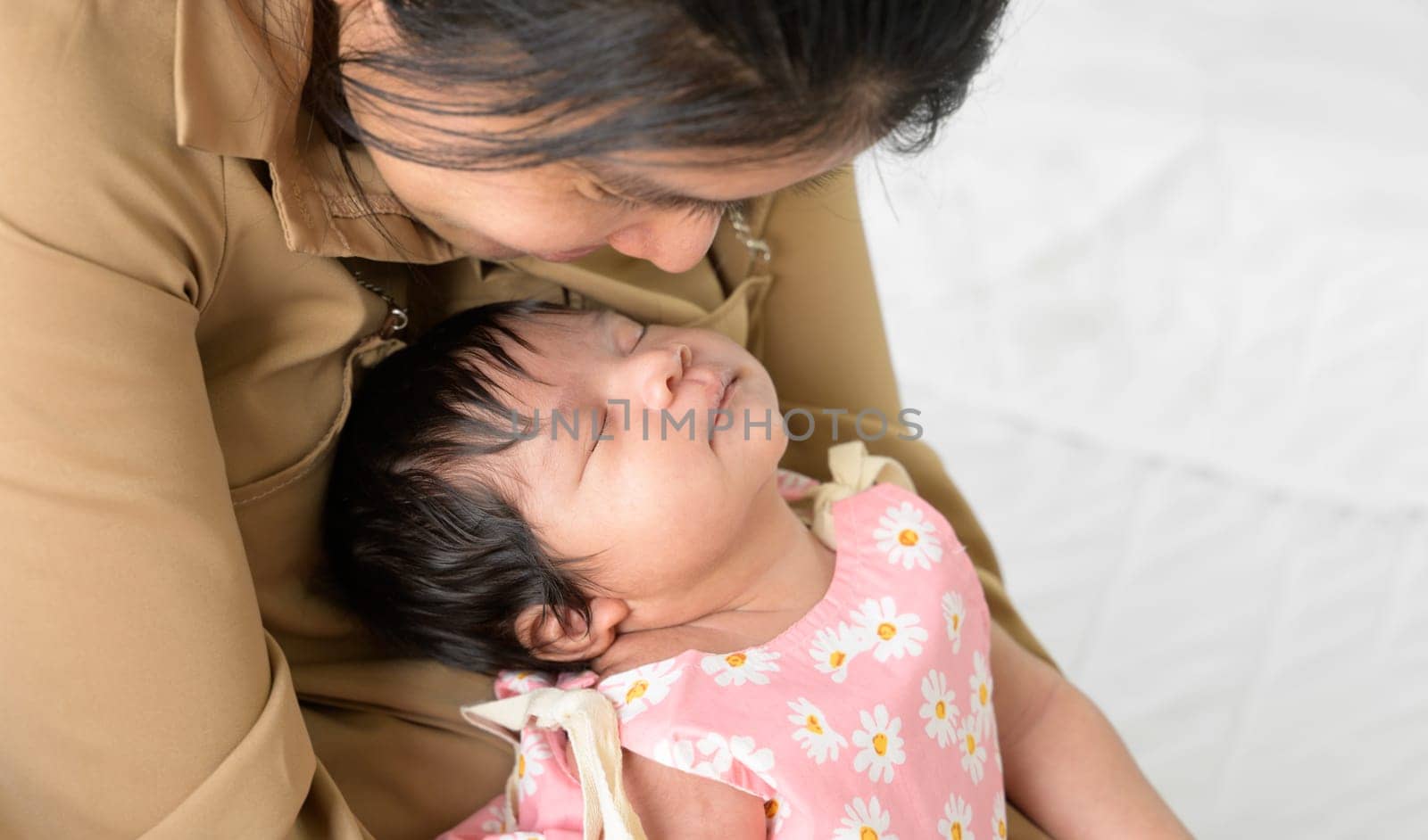 Happy newborn baby girl 1 month sleeping on mother arm. Mother sitting on whiet bed while nursing and looking her infant with love at home. Love, Health Care, love and mothers day concept
