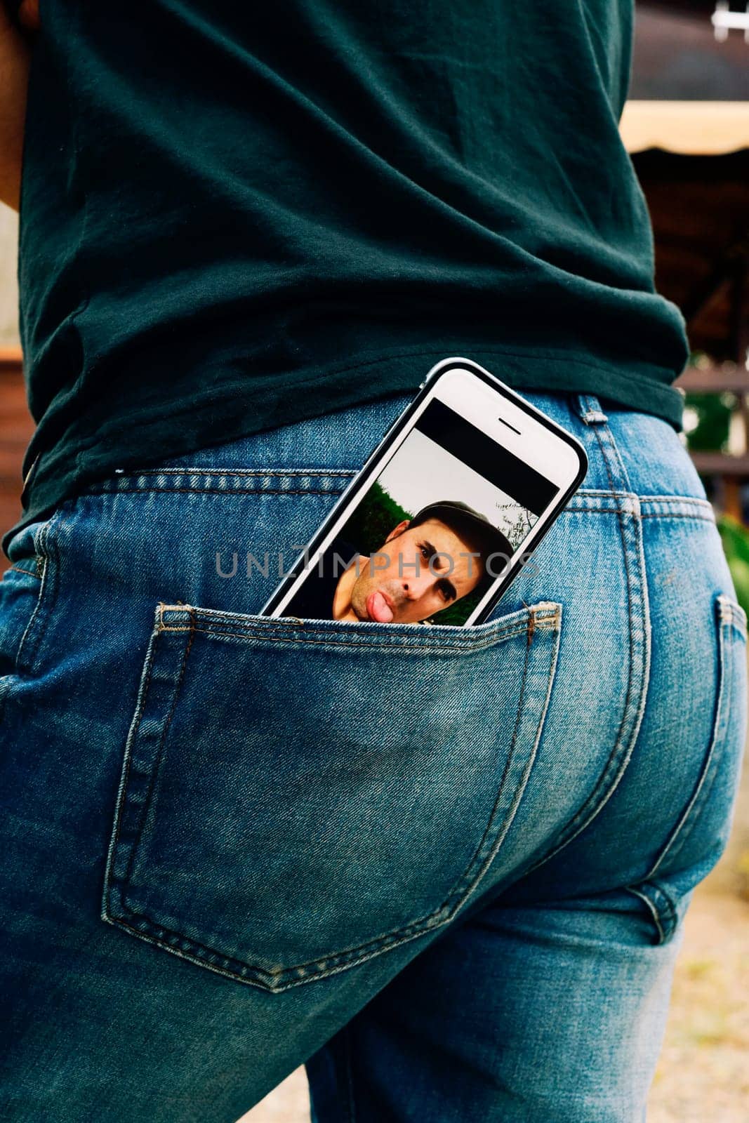 a smartphone with a picture of a young man sticking his tongue out in its screen, taken by myself, placed on the back pocket of the jeans of a young man