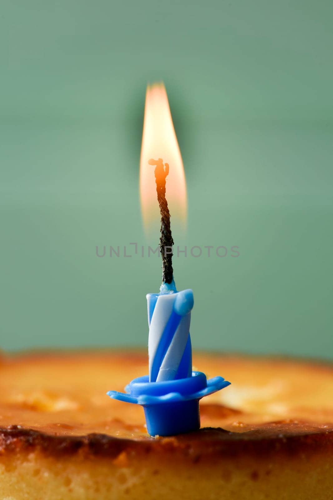 closeup of a cheesecake topped with a lit birthday candle against a rustic pale green wooden background