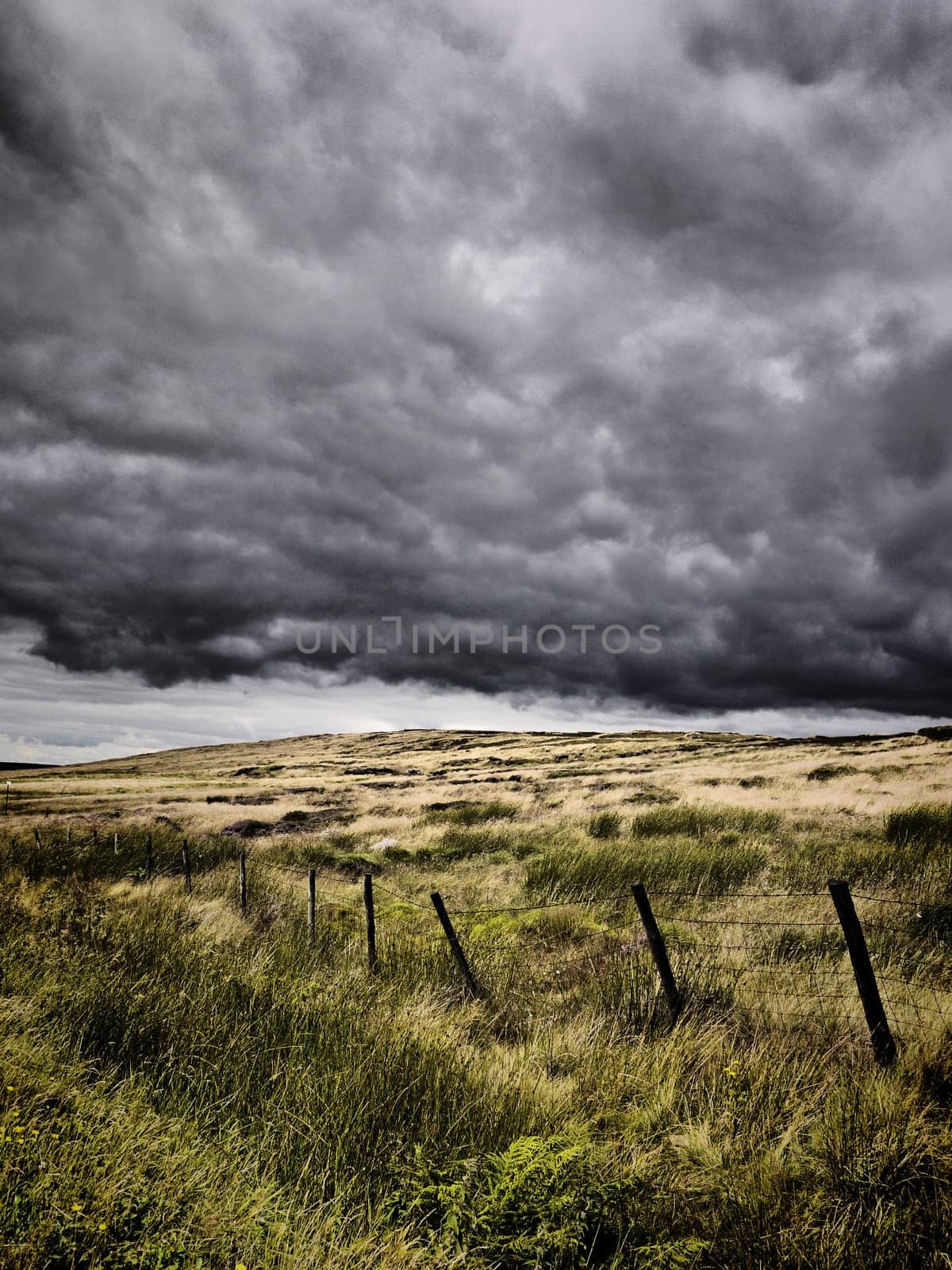 Intense looking clouds over a rural moorland. There is a poorly constructed fence running through the image.