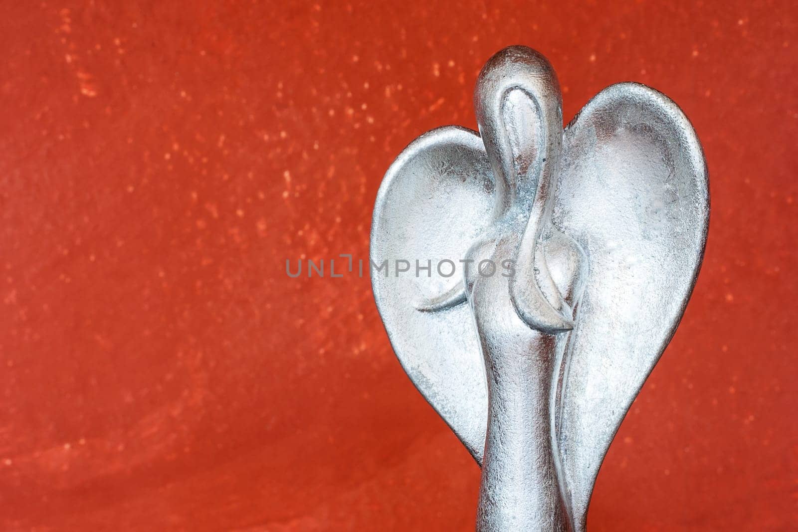 Upper body of a silver angel figure in front of terracotta colored wall