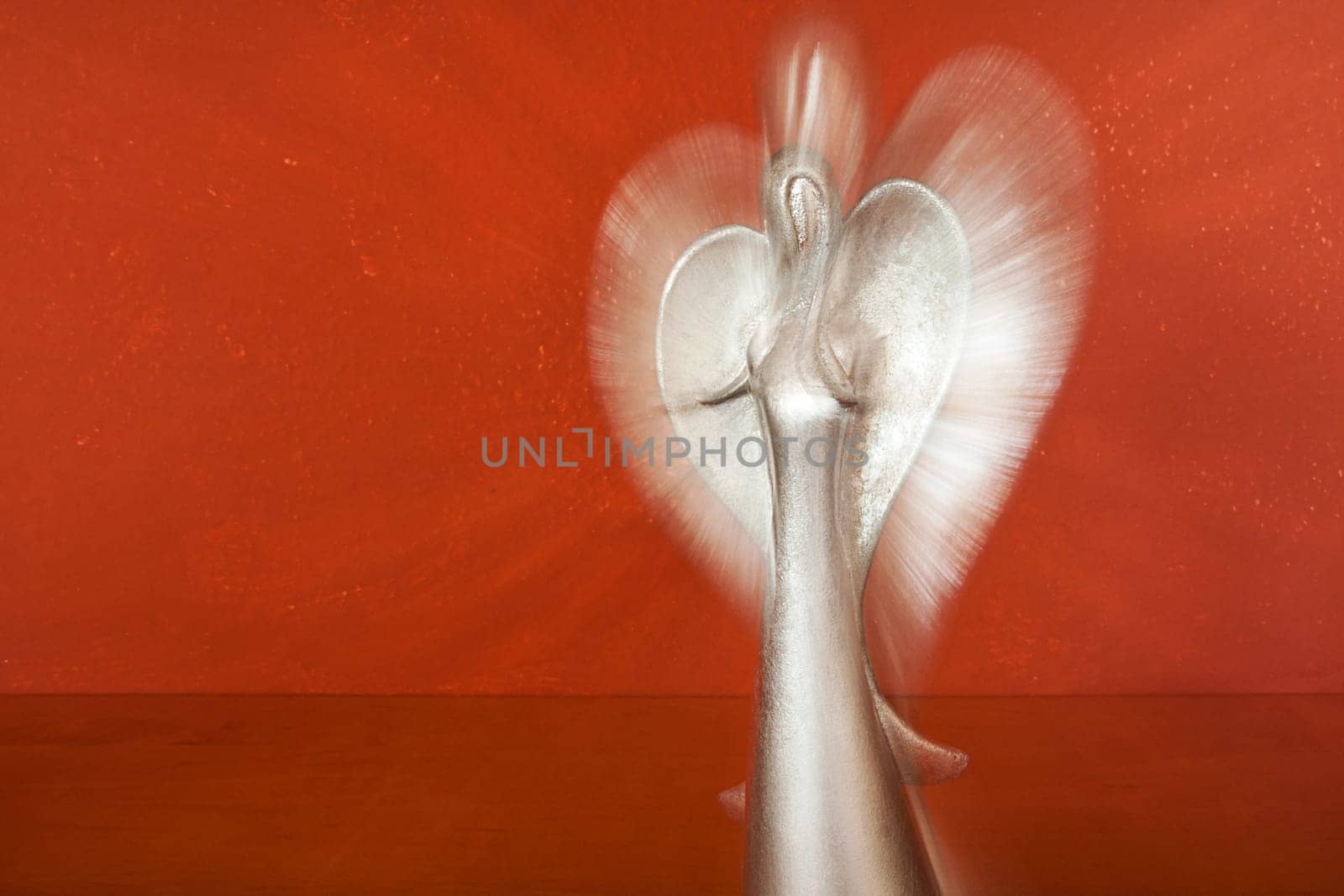 Upper body of a silver angel figure in front of terracotta colored wall with zoom effect
