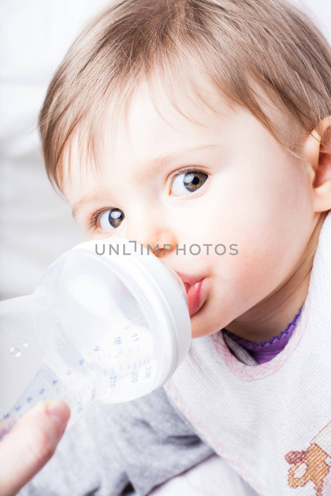 mother nursing her baby with a baby bottle while this little girl looks at the camera