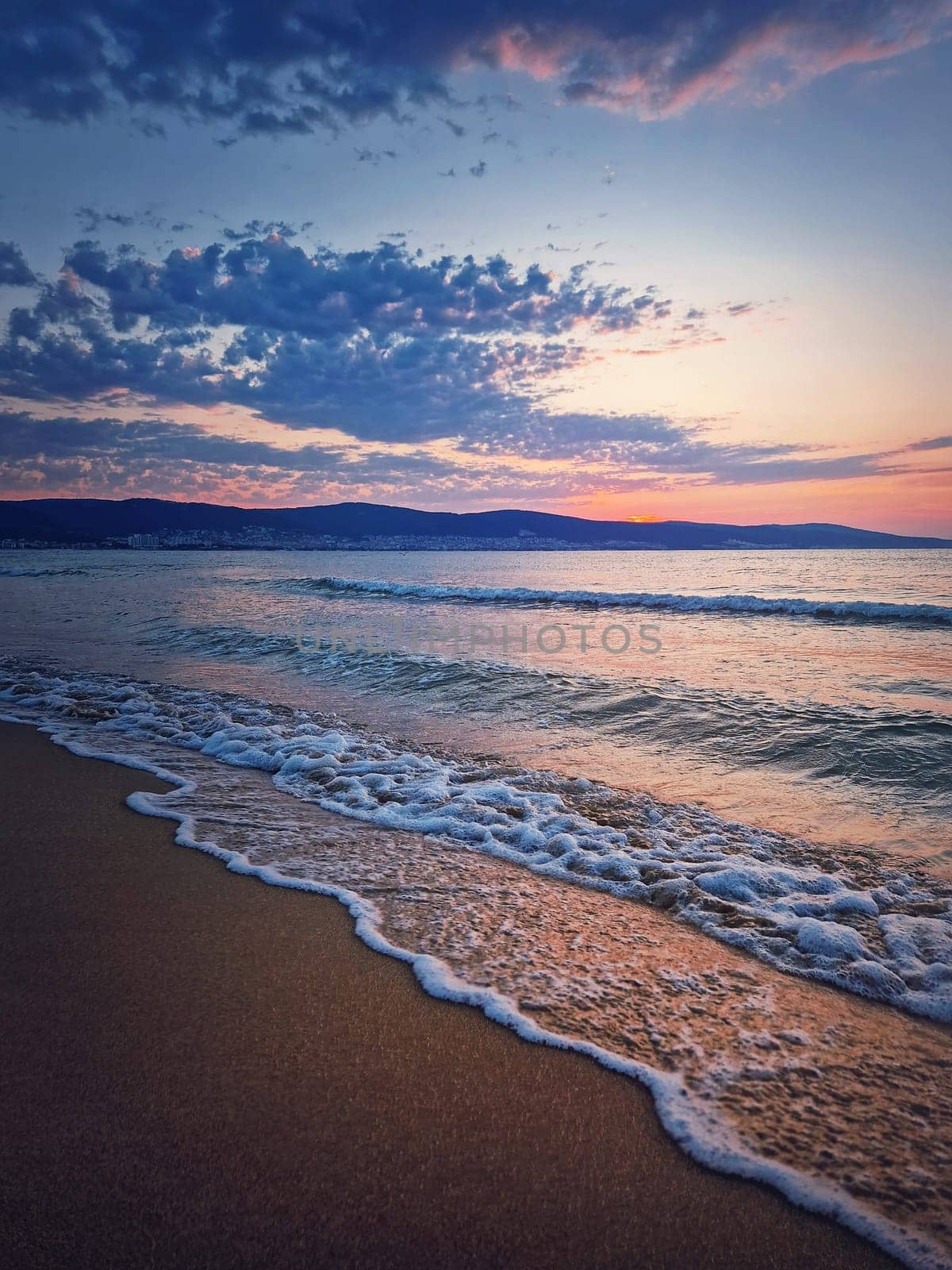 Sunrise at the sea with foamy waves on the sand and colorful sky at the horizon. Summer and travel background, Sunny Beach coastline in Bulgaria