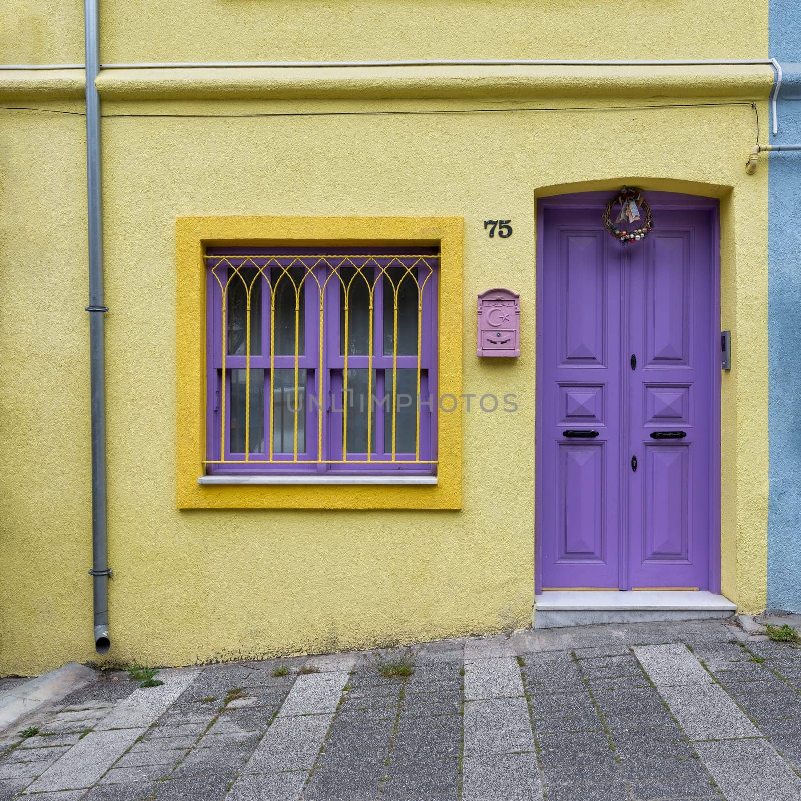 Exterior facade of residential building with walls painted in yellow and violet, Violet door, and wrought iron window, at a narrow street, Uskudar district, Istanbul, Turkey
