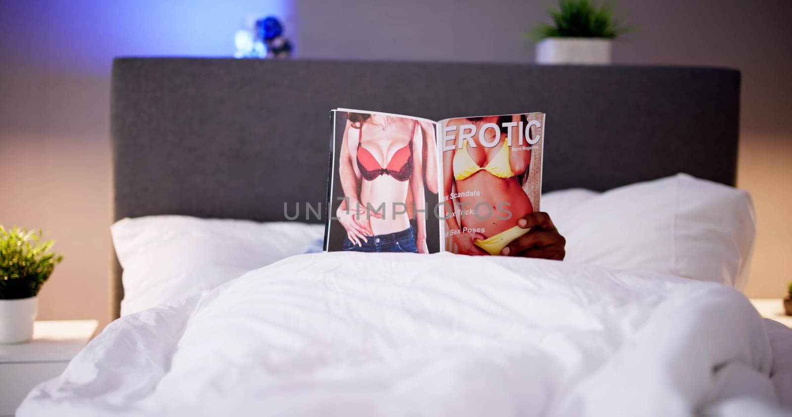 Man Lying On Bed Reading Erotic Magazine At Home