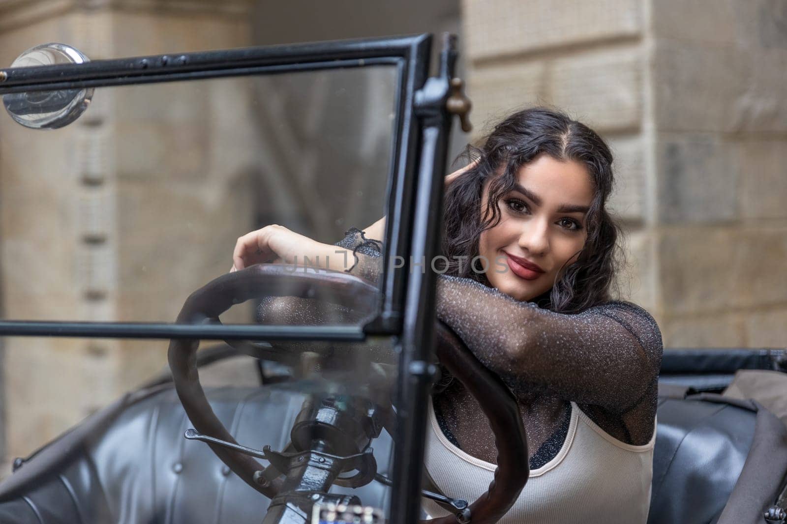 Attractive young woman with long black hair is posing on vintage car. Horizontally.