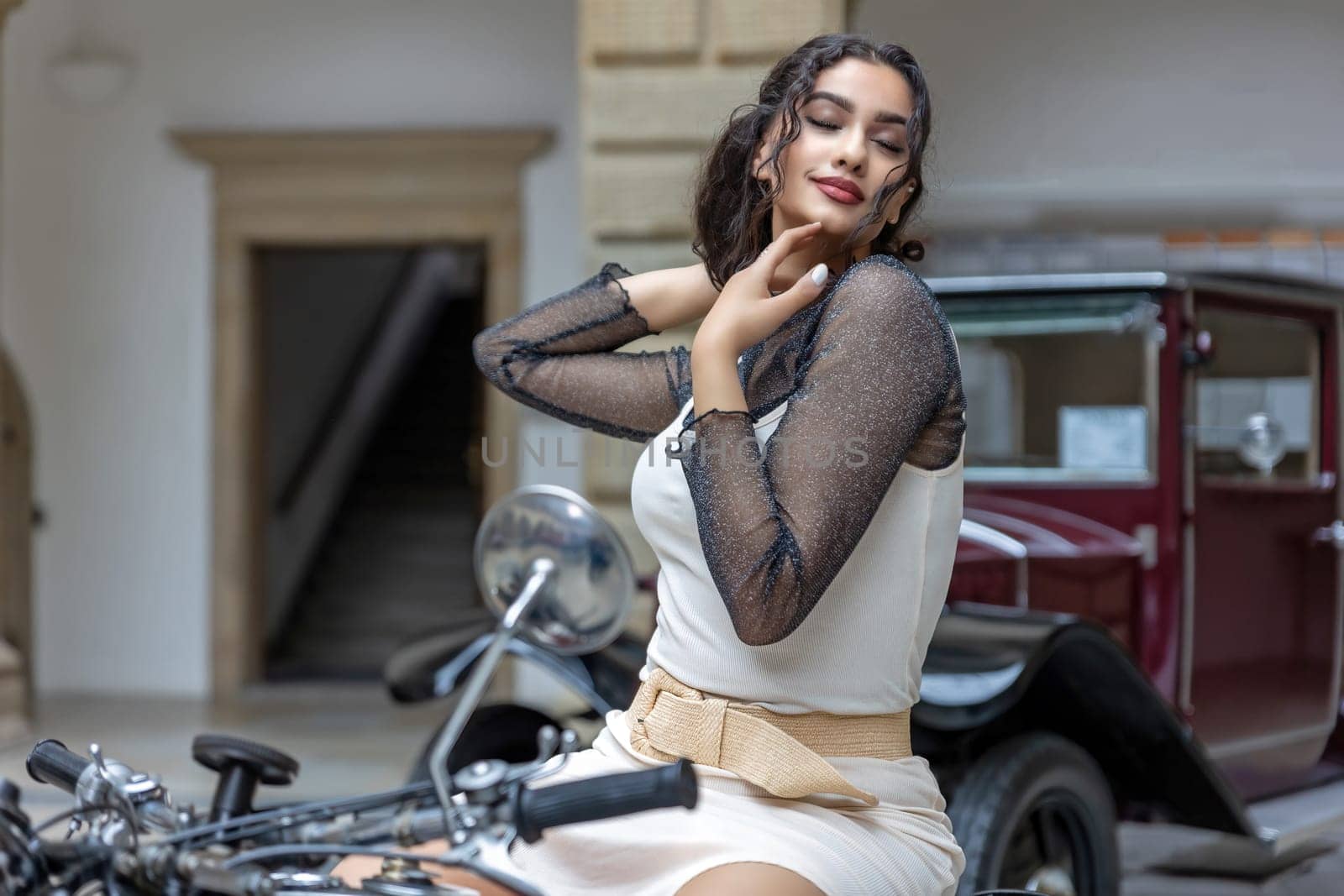 Young woman with long black  hair is sitting seductively on a vintage motorcycle. Horizontally.