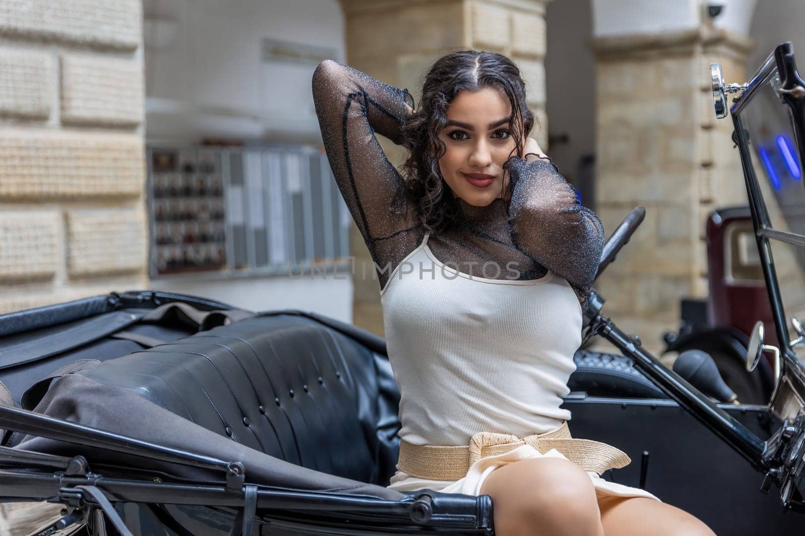 Beautiful long black hair young woman is looking at the camera sitting on vintage car . Horizontally.