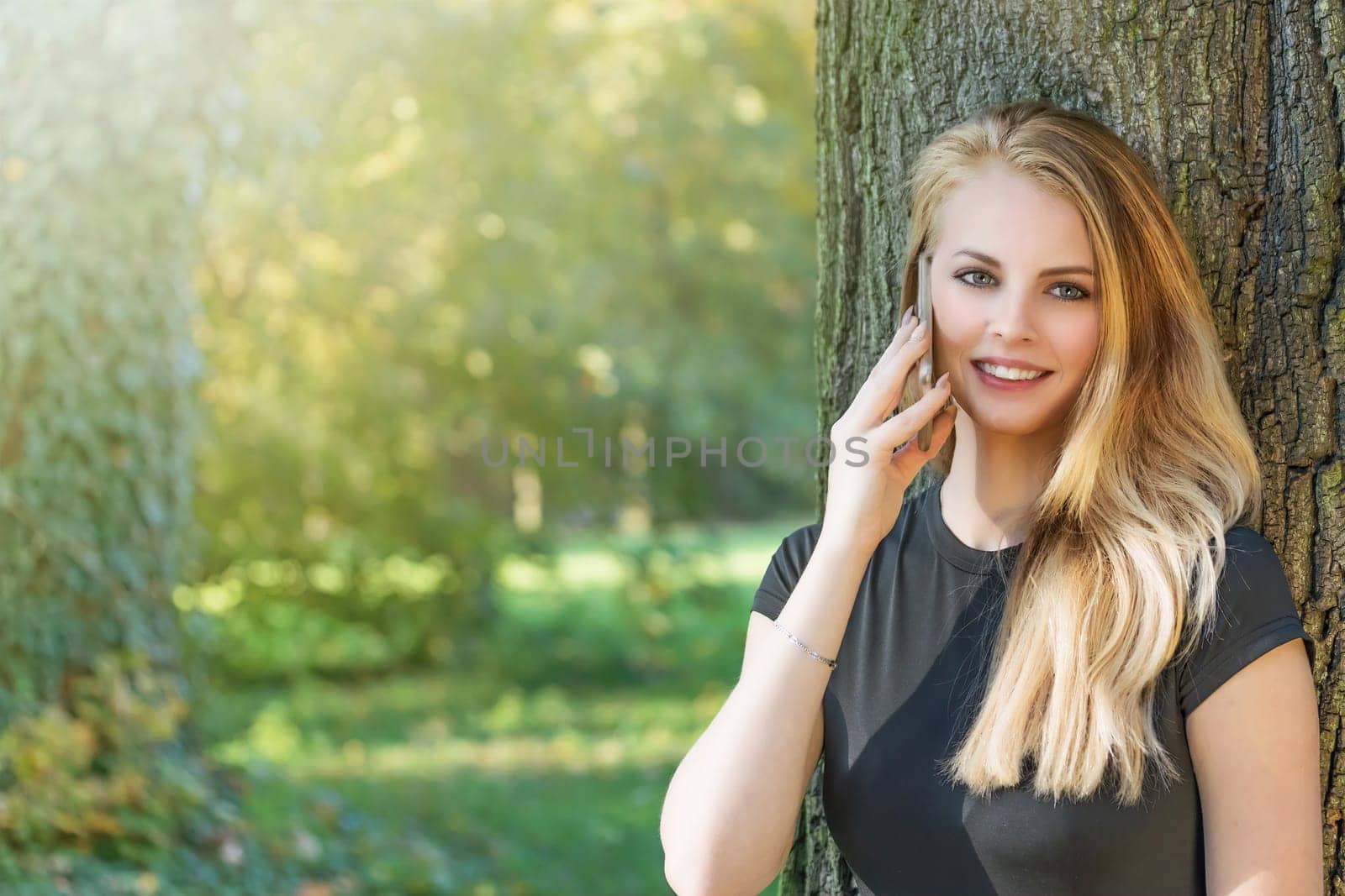 Attractive long haired young girl is on the phone outdoors . Horizontally.