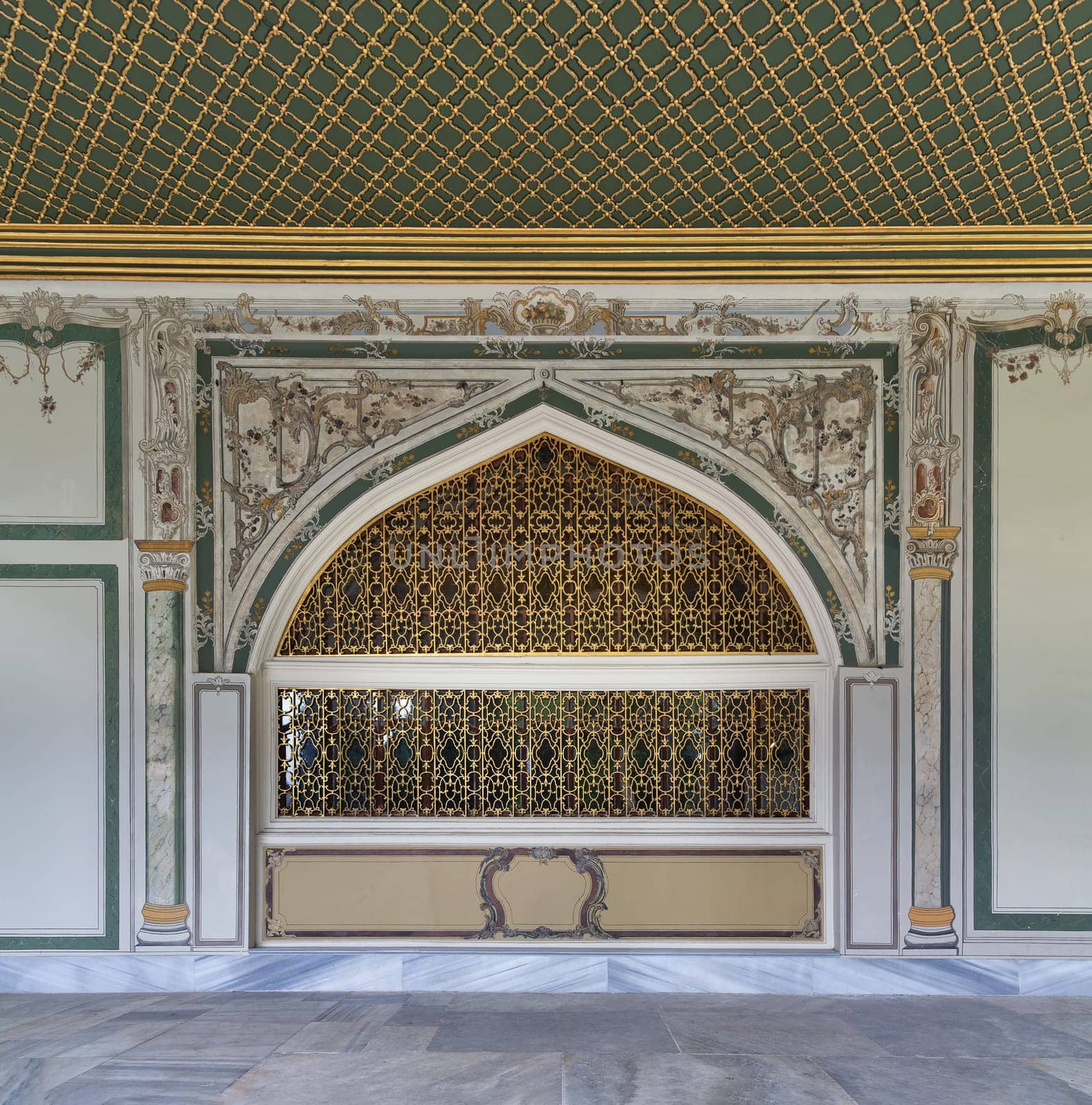 Golden decorated wrought iron arched windows in painted ornate wall and green decorated ceiling at the courtyard of Dolmabahce Palace, Besiktas district, Istanbul, Turkey