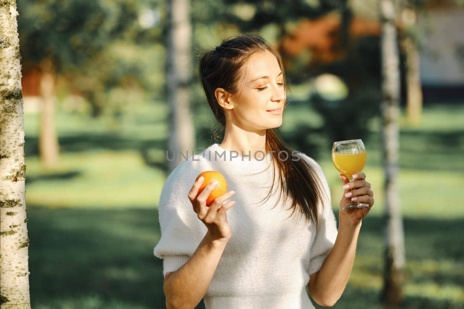 Woman holds orange in one hand and glass of orange juice in other
