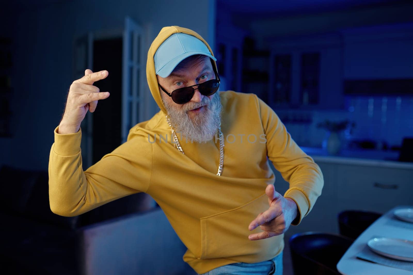 Funky senior man in modern casual clothes dancing hip hop for camera at home kitchen