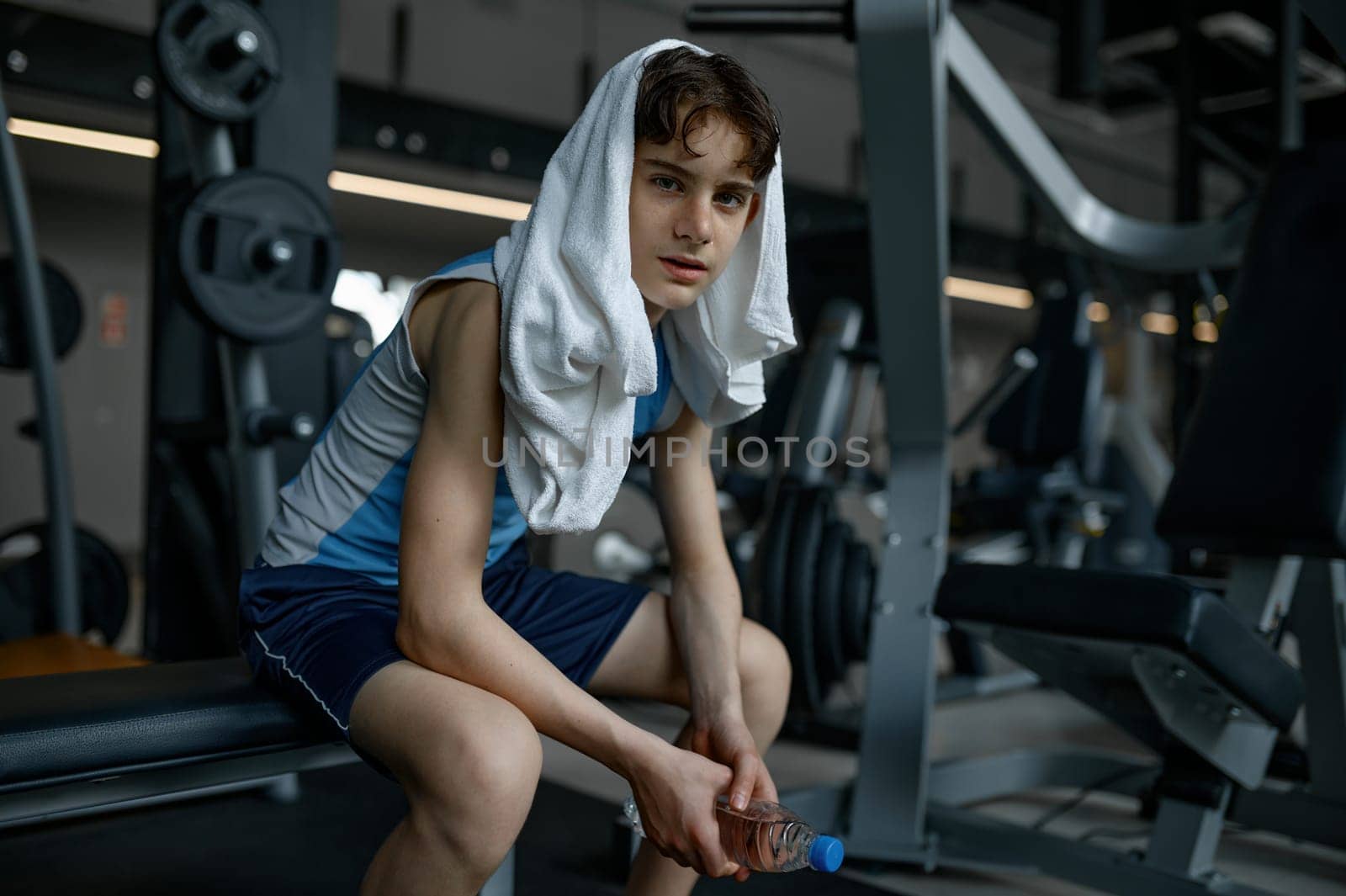 Portrait of sweaty teenager boy with towel on head rest after training at gym. Sport, hobby and healthy lifestyle for children