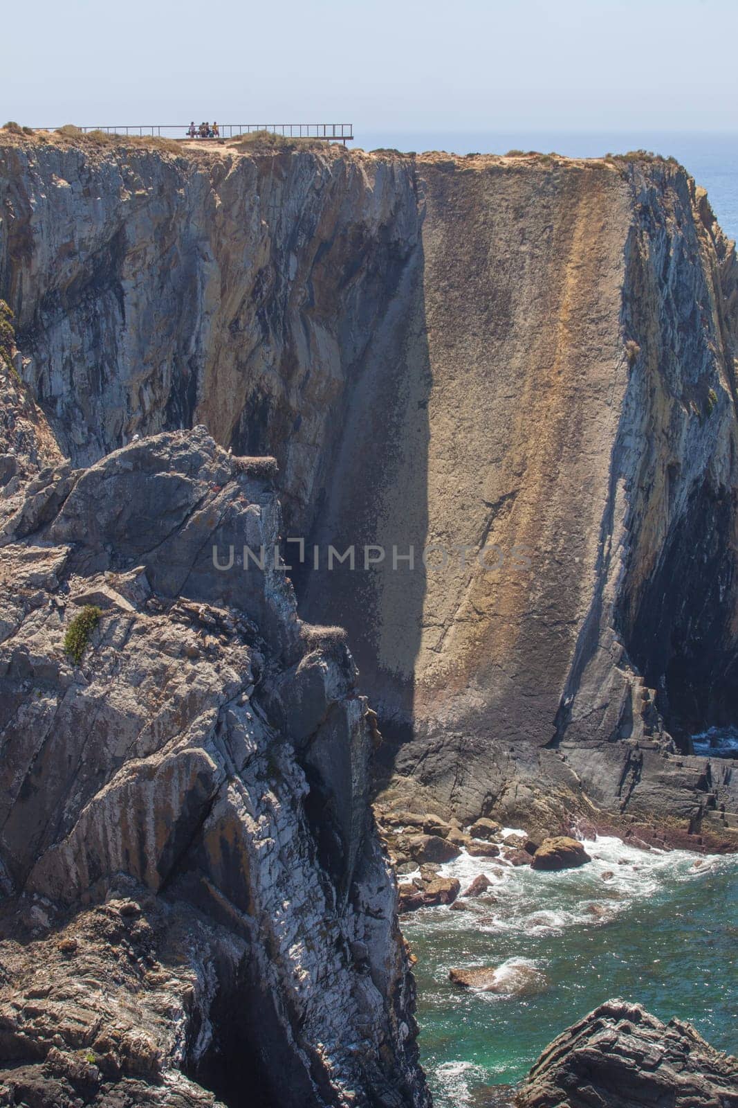 Visitors sitting on bench close to cliffs of Cabo Sardao coast, Ponta do Cavaleiro, Sao Teotonio, Portugal