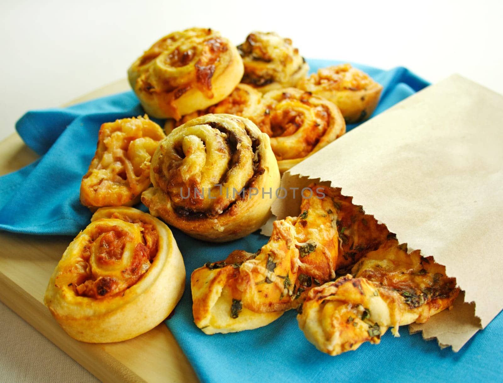 A selection of baked treats including tomato and herb sticks in a paper bag and baked scrolls.