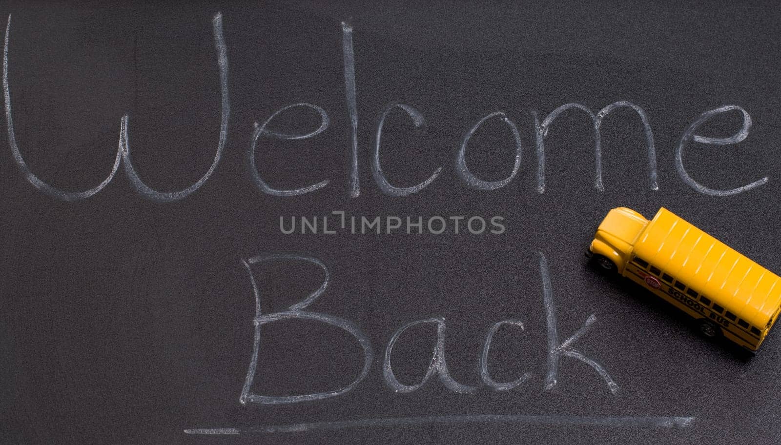 A black board with the words welcome back, and also a small toy school bus