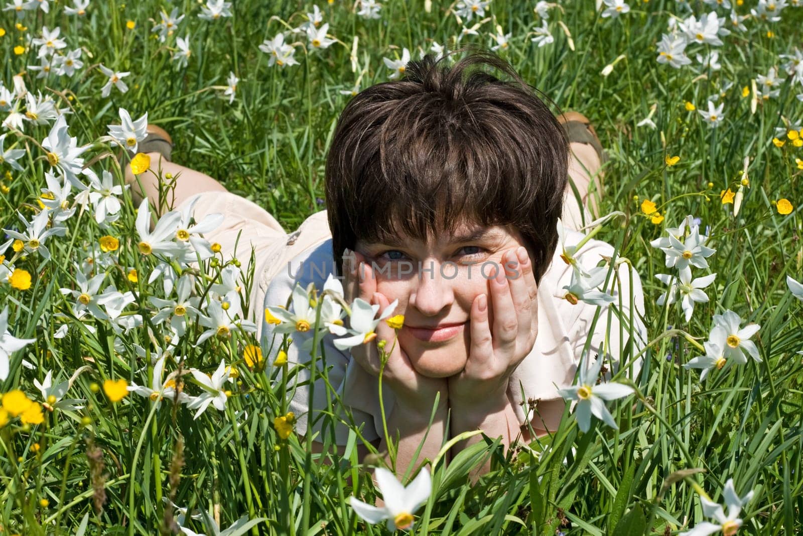 Beatiful woman leaning on her elbows in green grass among the flowers